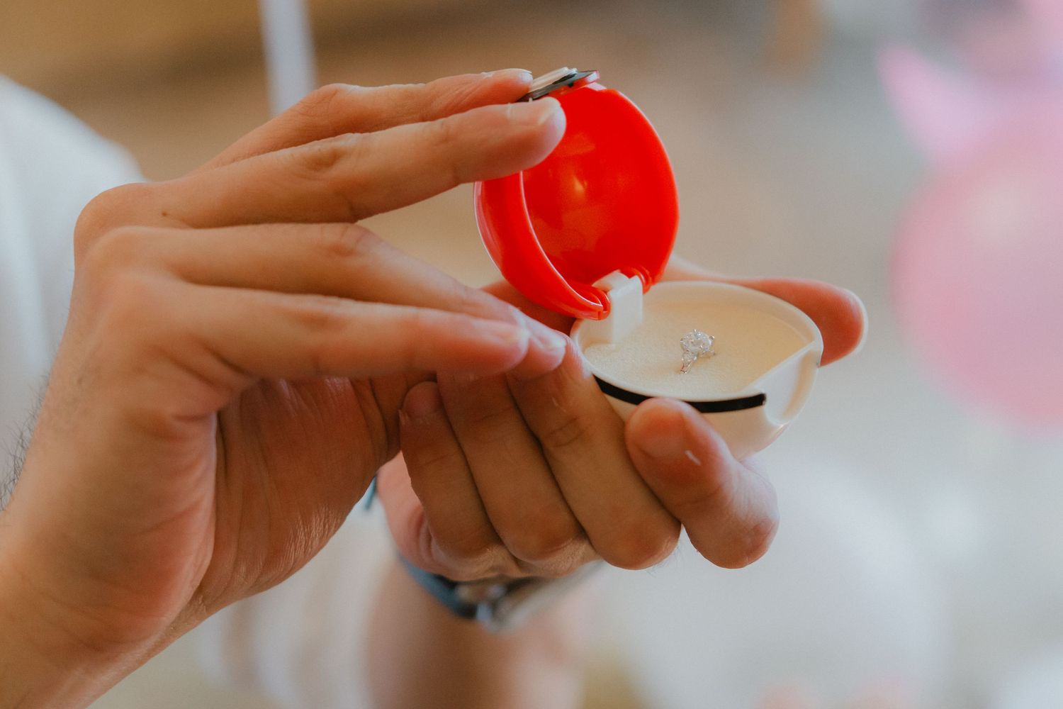 Close-up shot of hands exchanging a small red box during a proposal moment.