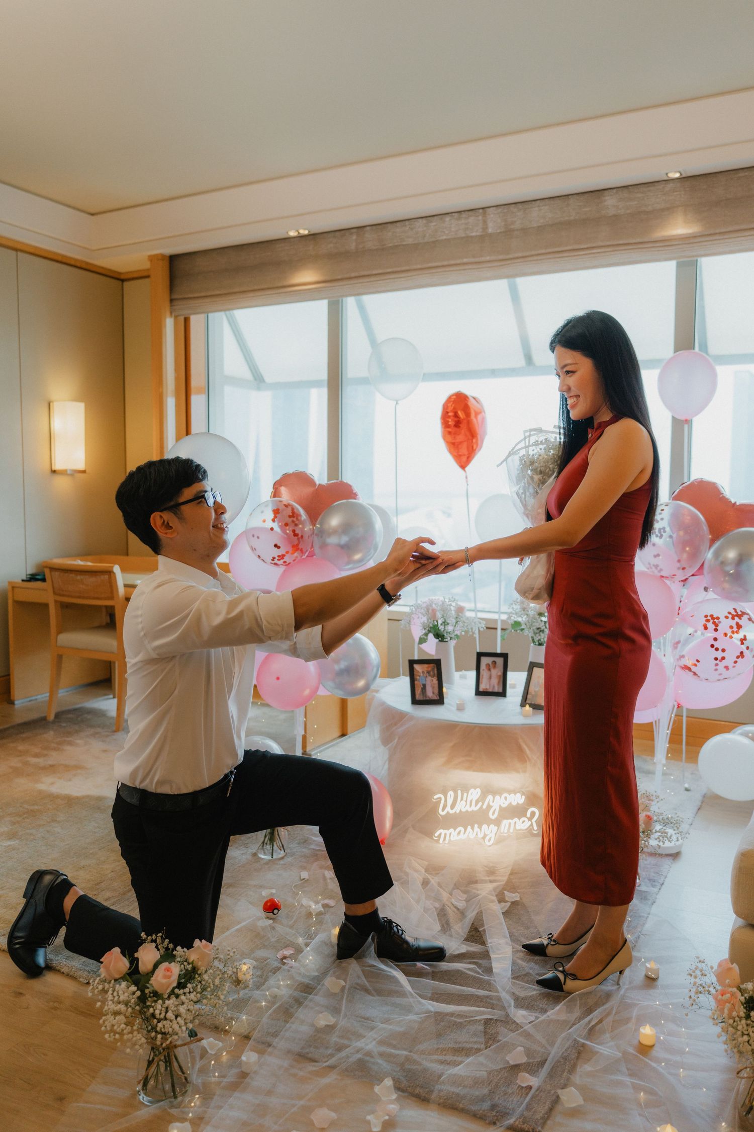 A romantic marriage proposal scene with red balloons and decorations in an elegant indoor setting.