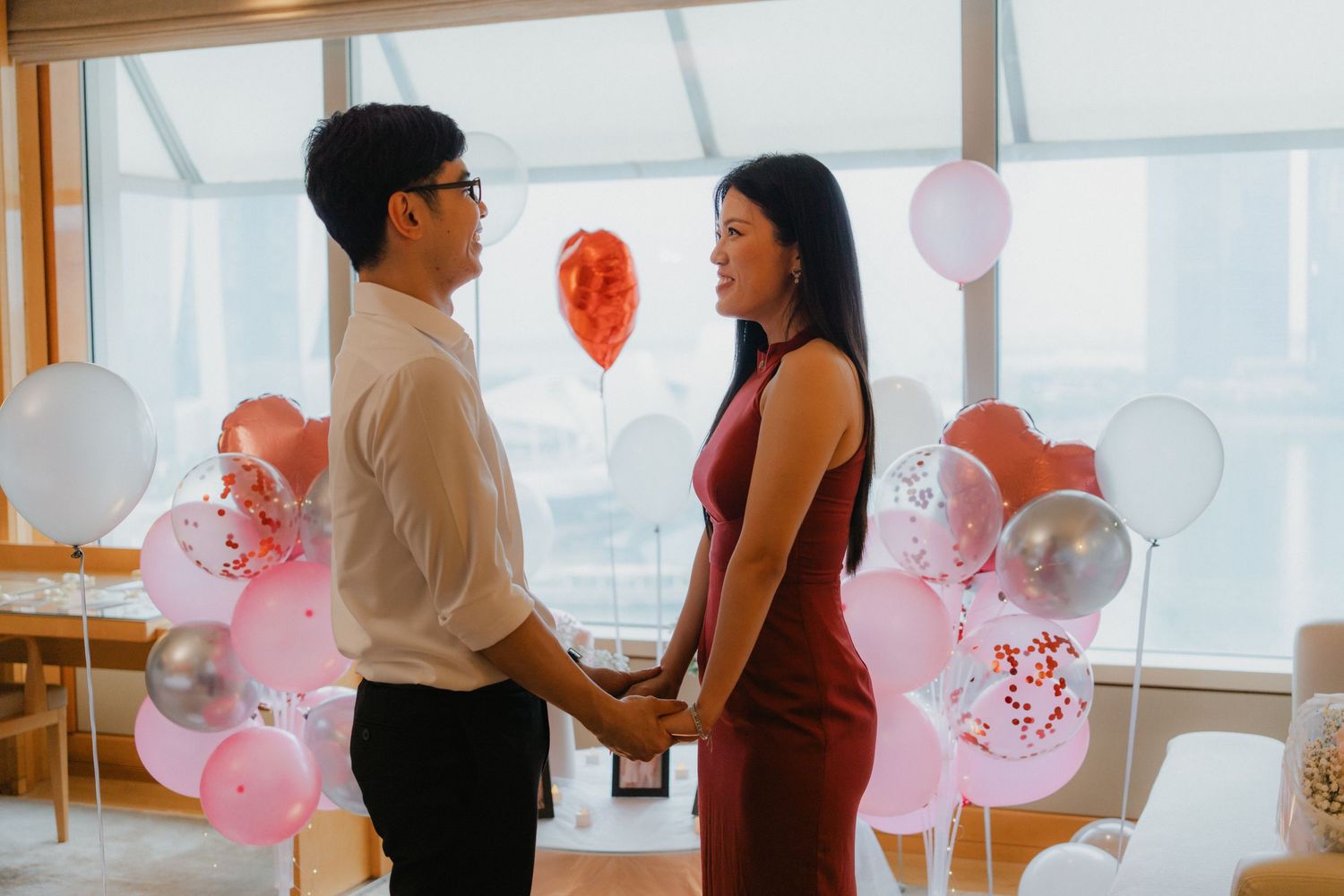 A couple celebrating their engagement in a room decorated with pink and white balloons.