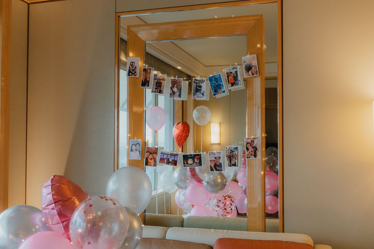 A mirror displays photos hanging on string with pink and white balloons scattered in the reflection.