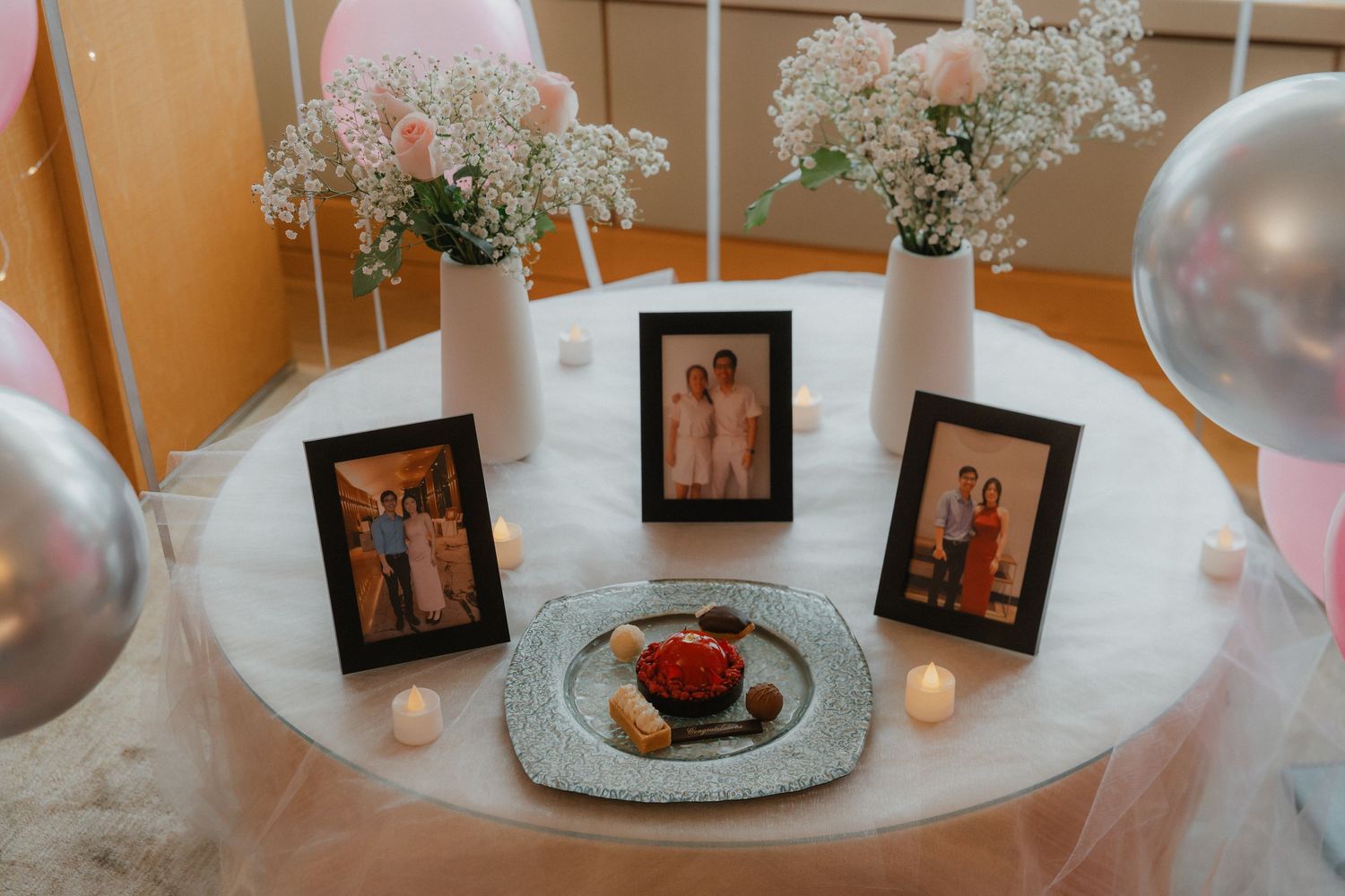 Elegant table decor with framed photos, white flowers and silver balloons for a proposal.