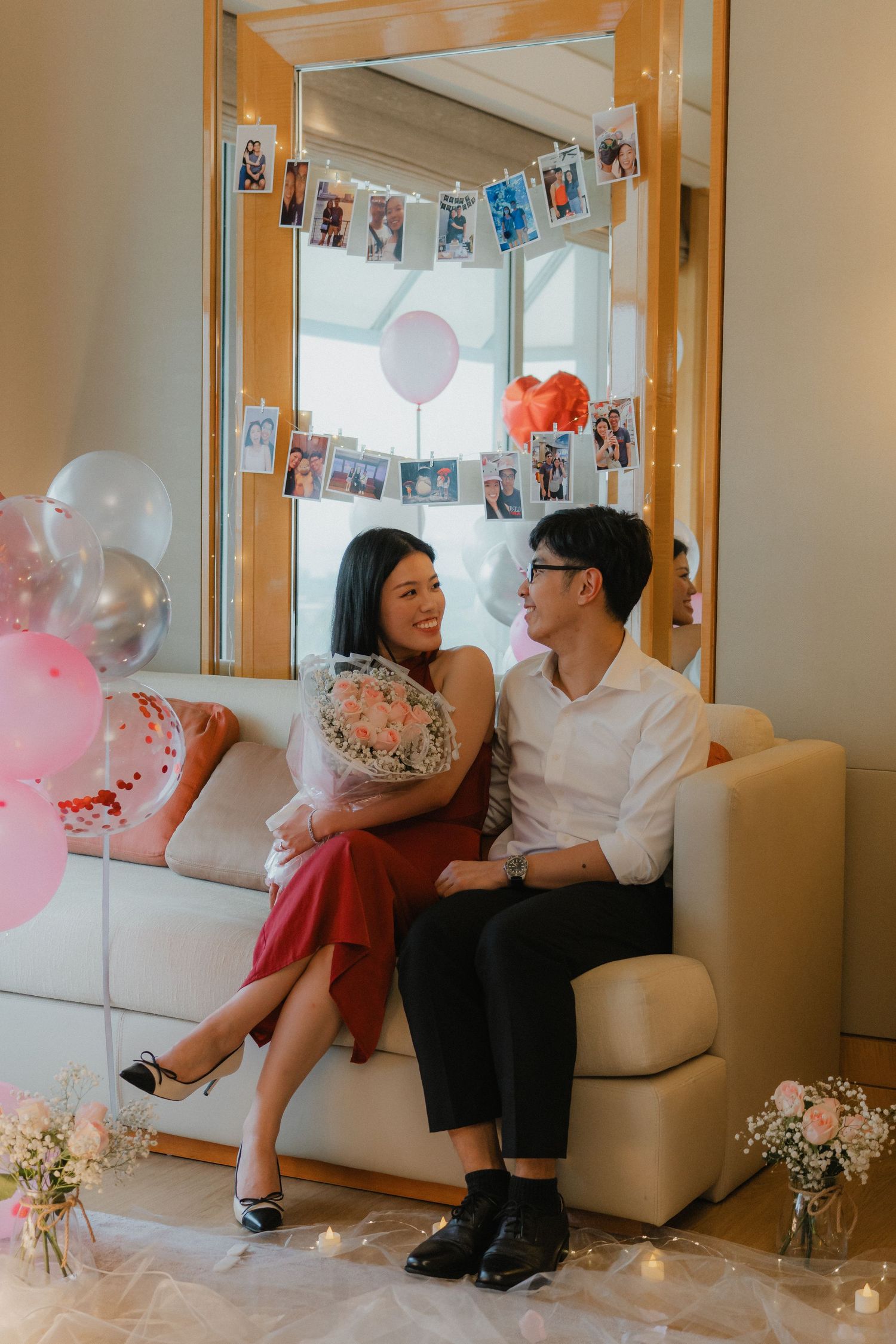 Couple sharing a tender moment on a couch surrounded by romantic decor and photo displays.
