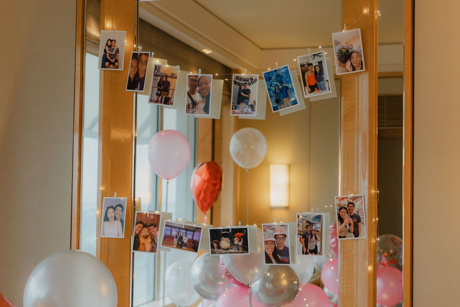 Polaroid photos hang on string with pink balloons and party decorations in warm interior lighting.