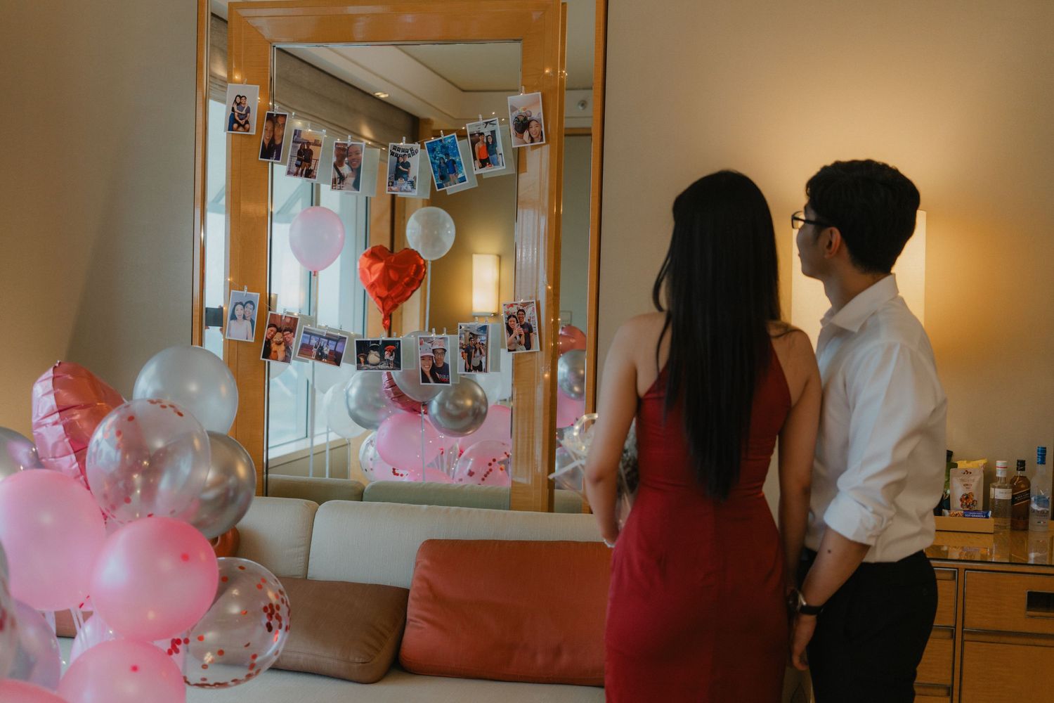 Couple admires photo display in romantically decorated room with pink balloons.