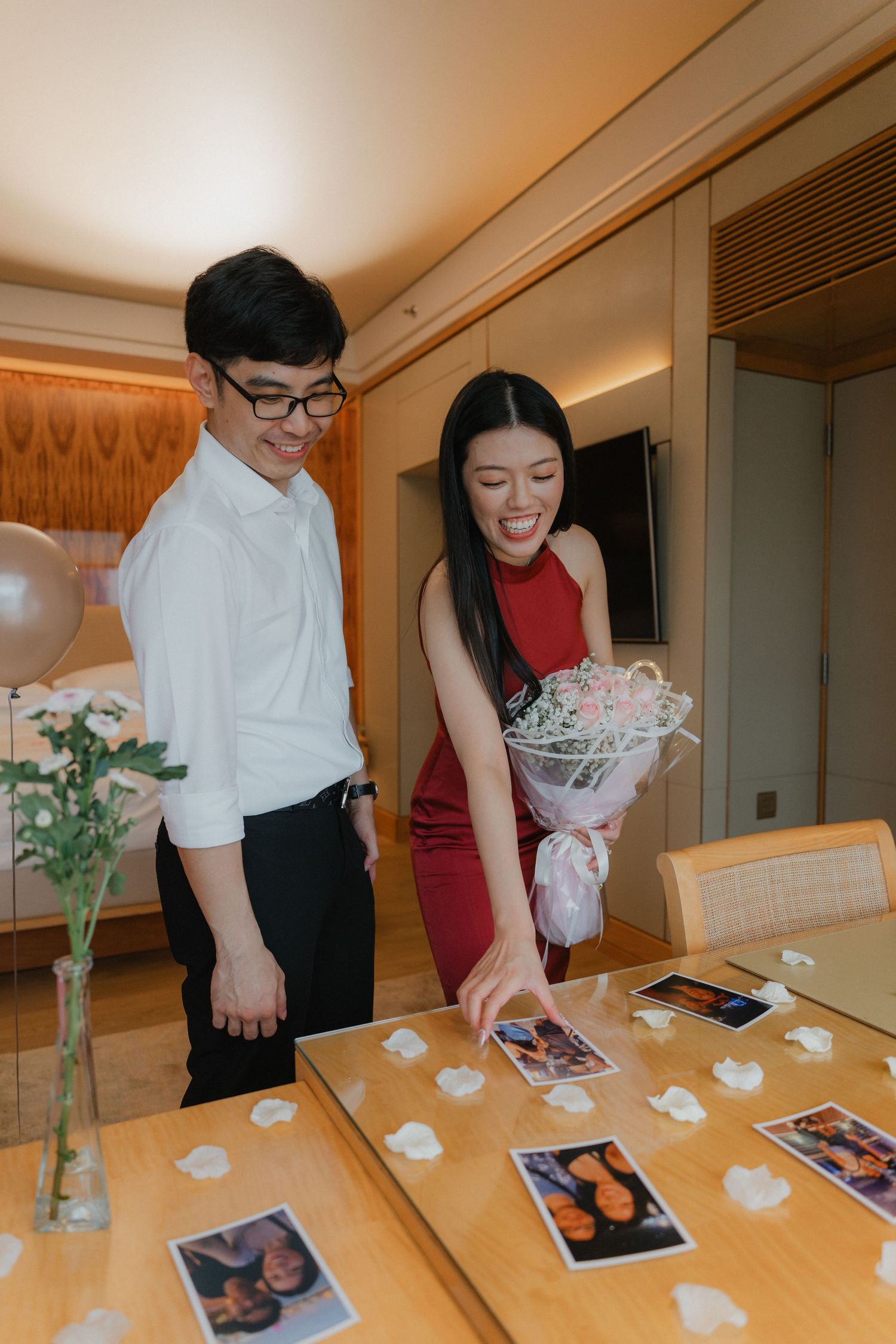 Intimate indoor celebration with balloons, flowers and photographs displayed on wooden table.