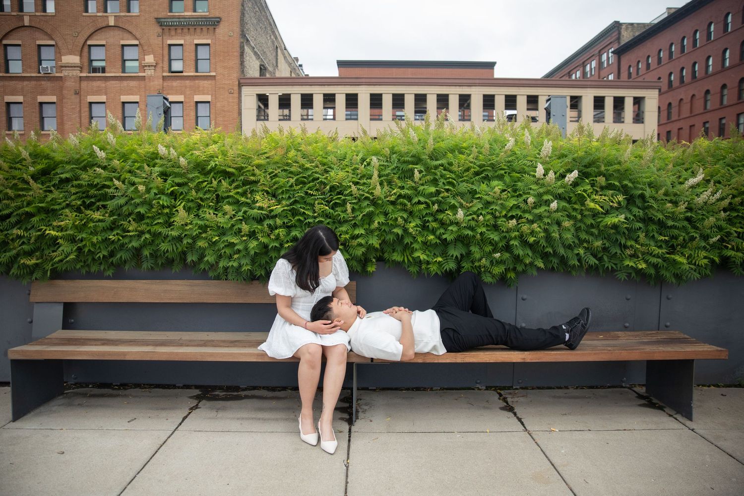 A couple relaxes on stone benches along the New York City High Line park with urban architecture in the background.