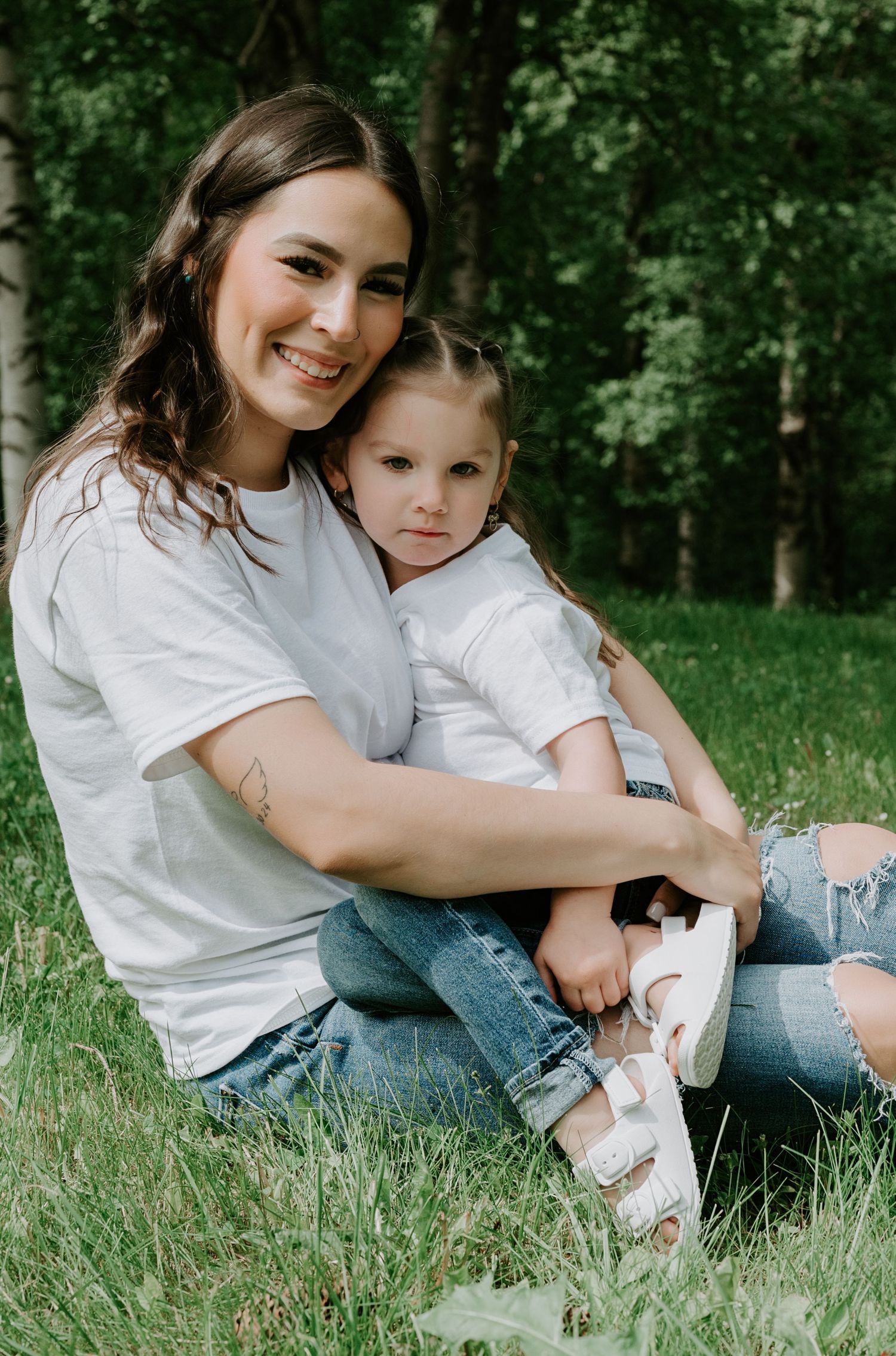 A tender outdoor portrait showing matching white shirts and ripped jeans while sitting in green grass.
