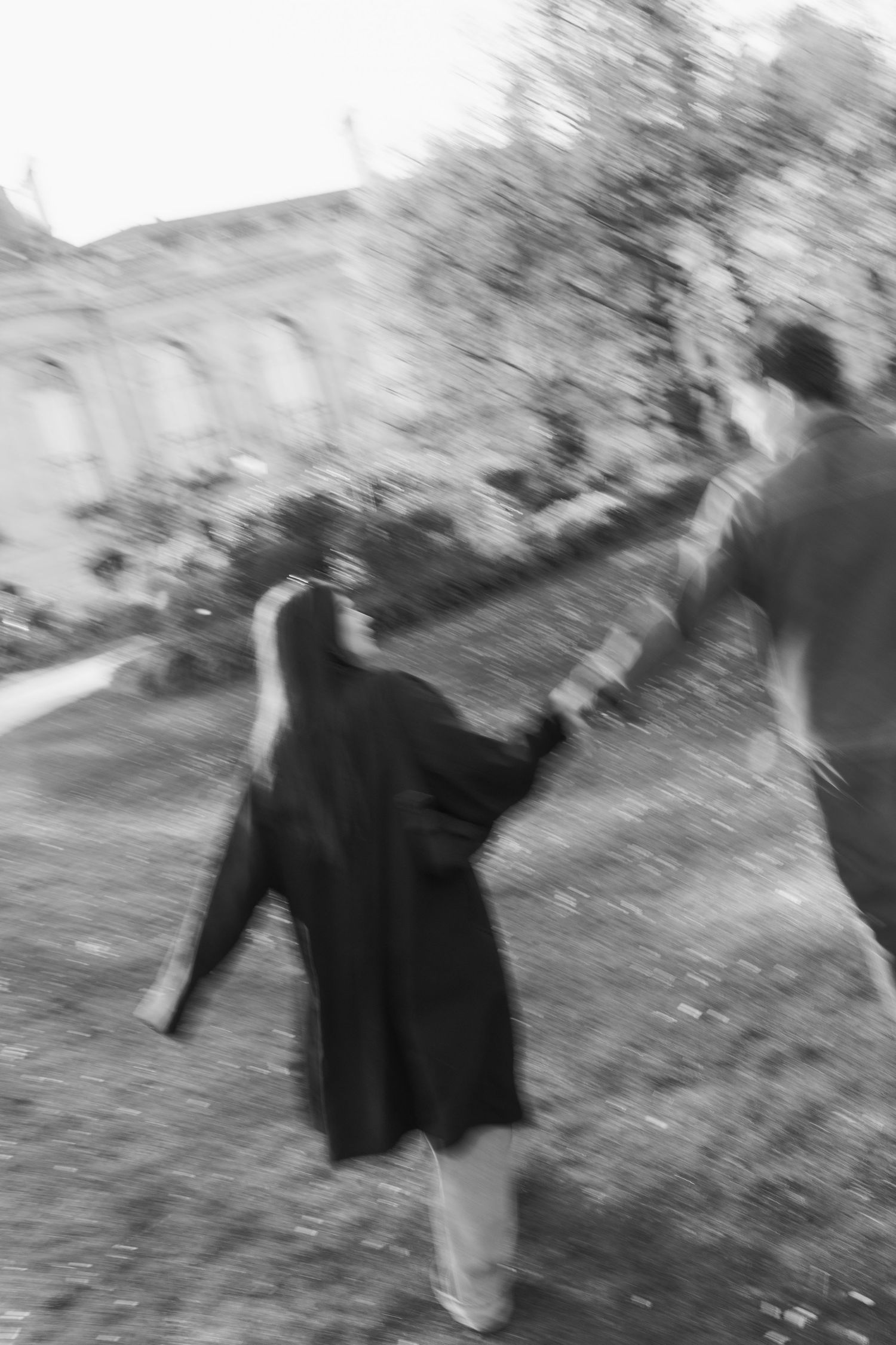 A blurred black and white photo of a person in dark clothing walking outdoors along a path.