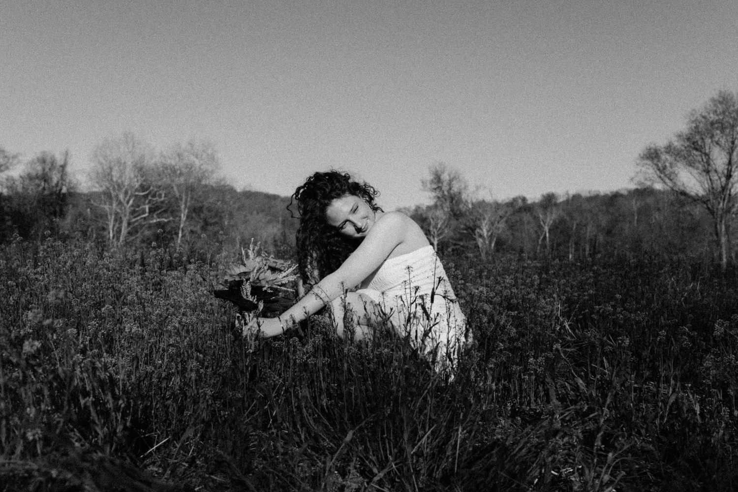 A black and white artistic portrait of someone sitting among tall grasses in Frederick Maryland