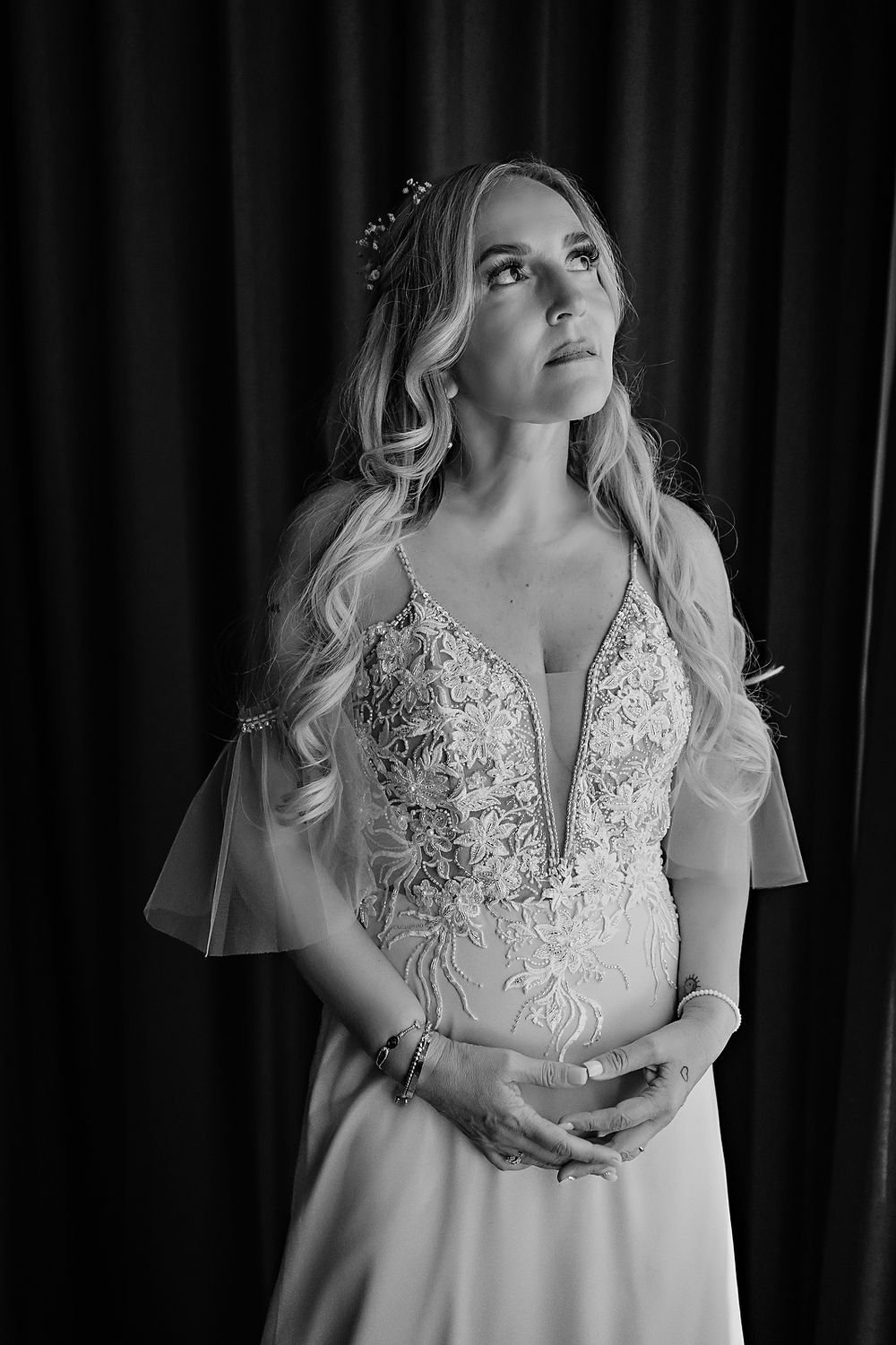 Black and white portrait of bride in lace wedding dress with flowy sleeves looking upward thoughtfully.