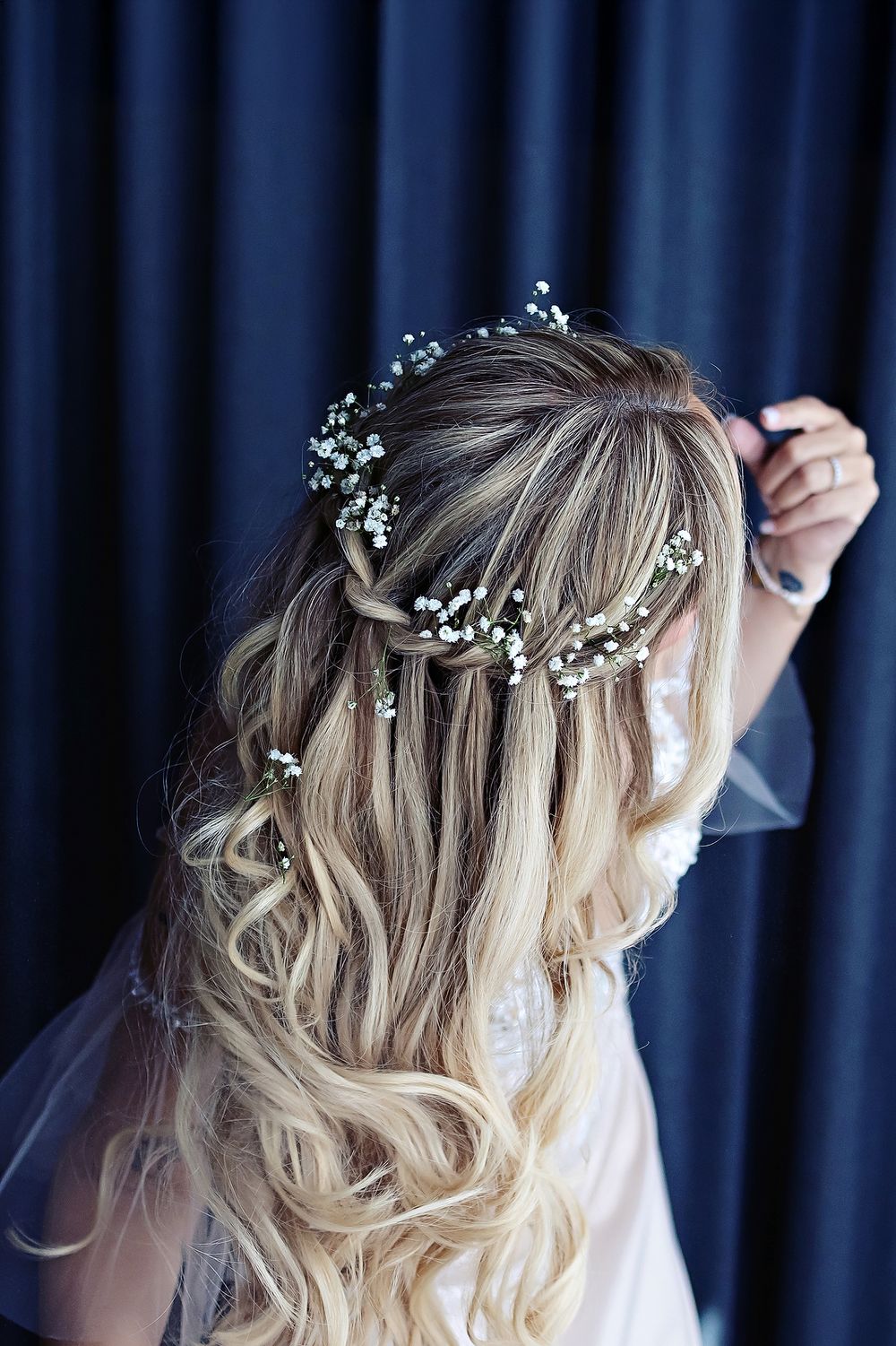 Small white flowers delicately placed in wavy blonde hair styled in a romantic boho look against a navy background.