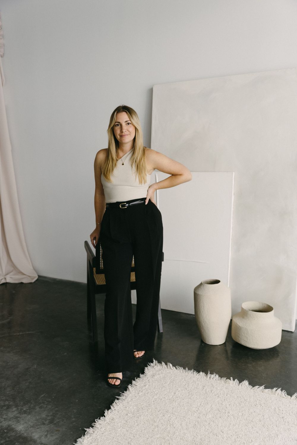 Modern fashion studio portrait showcasing high-waisted black pants and white top with minimalist decor and pottery.