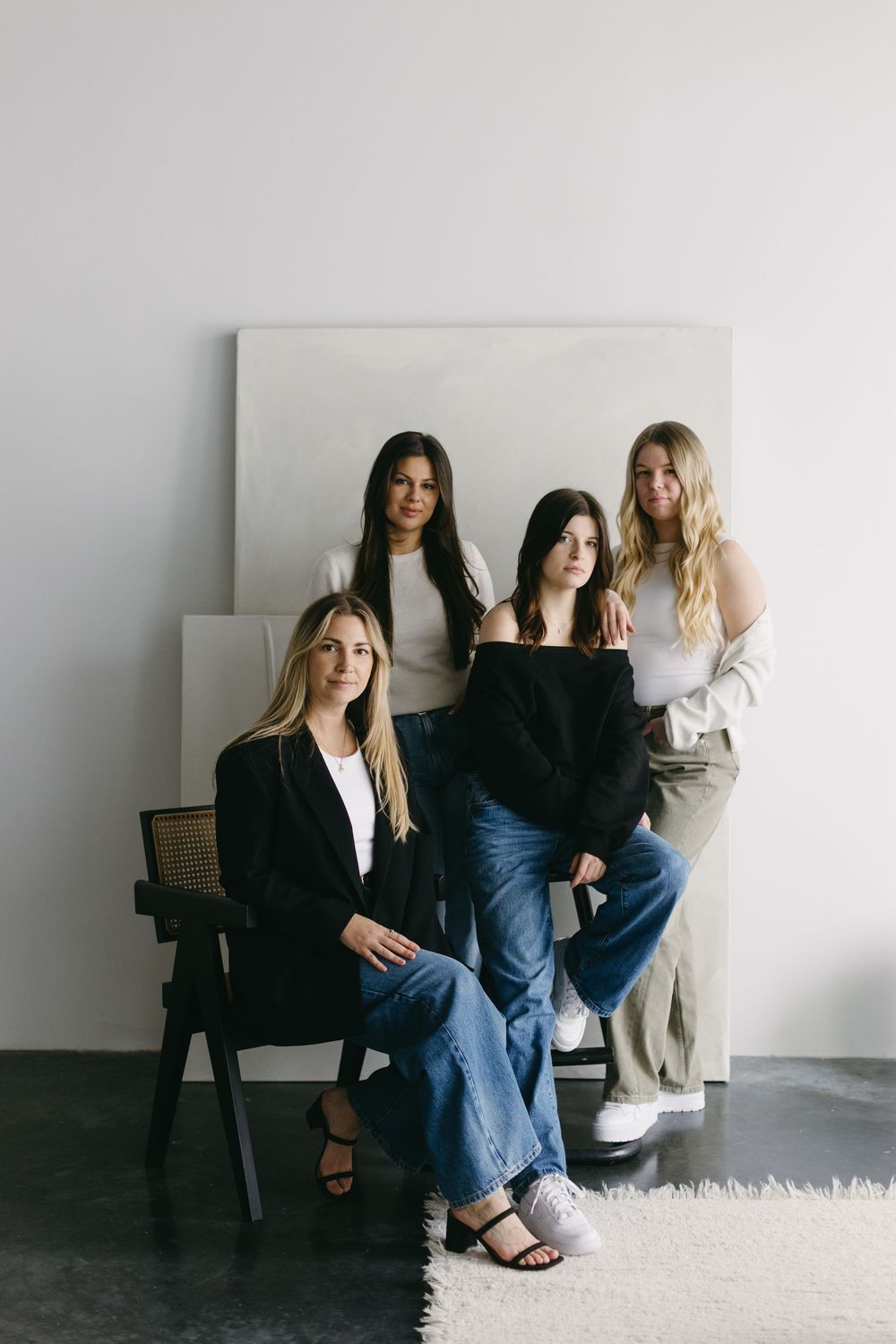 Four women in casual outfits pose together in a minimalist white studio setting, creating a modern lifestyle portrait.