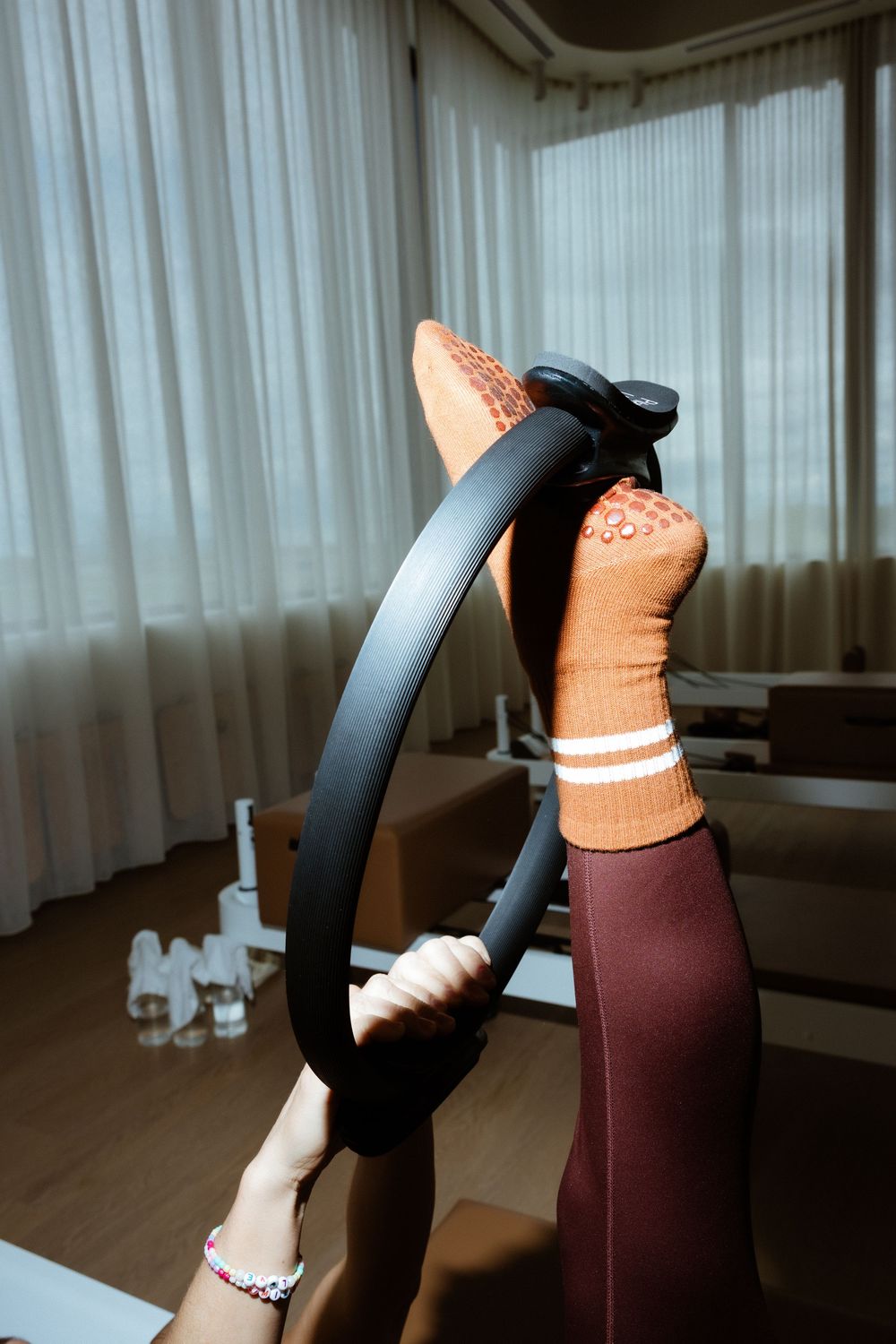 Legs in burgundy leggings and peach socks doing yoga poses against hardwood floor and white curtains in a sequence.