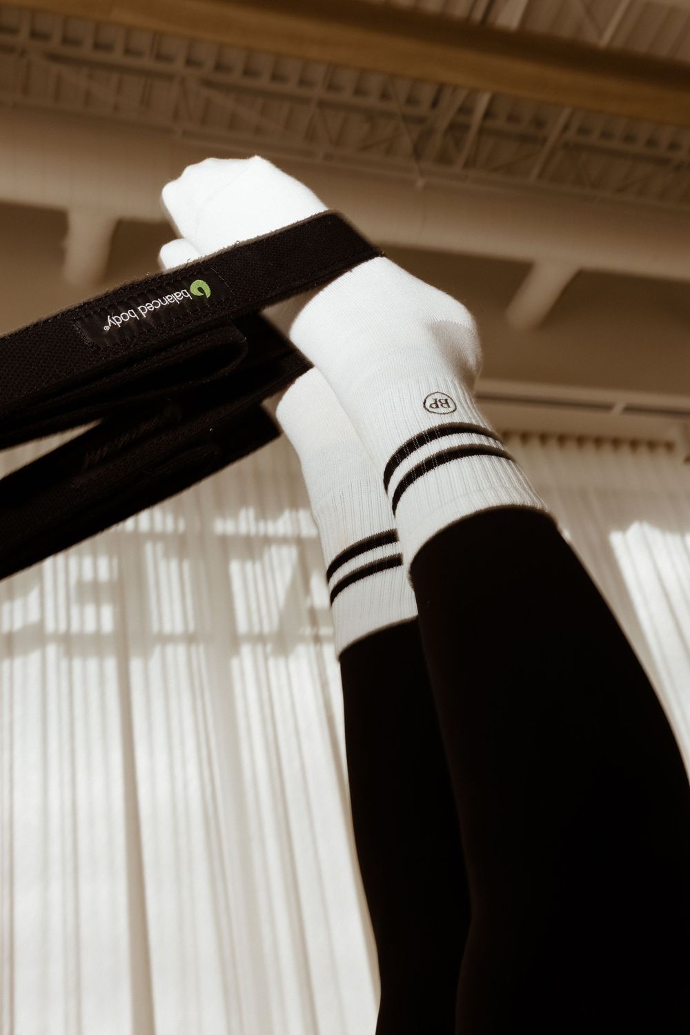 Close-up view of black and white striped athletic socks against a sunlit curtained window background.