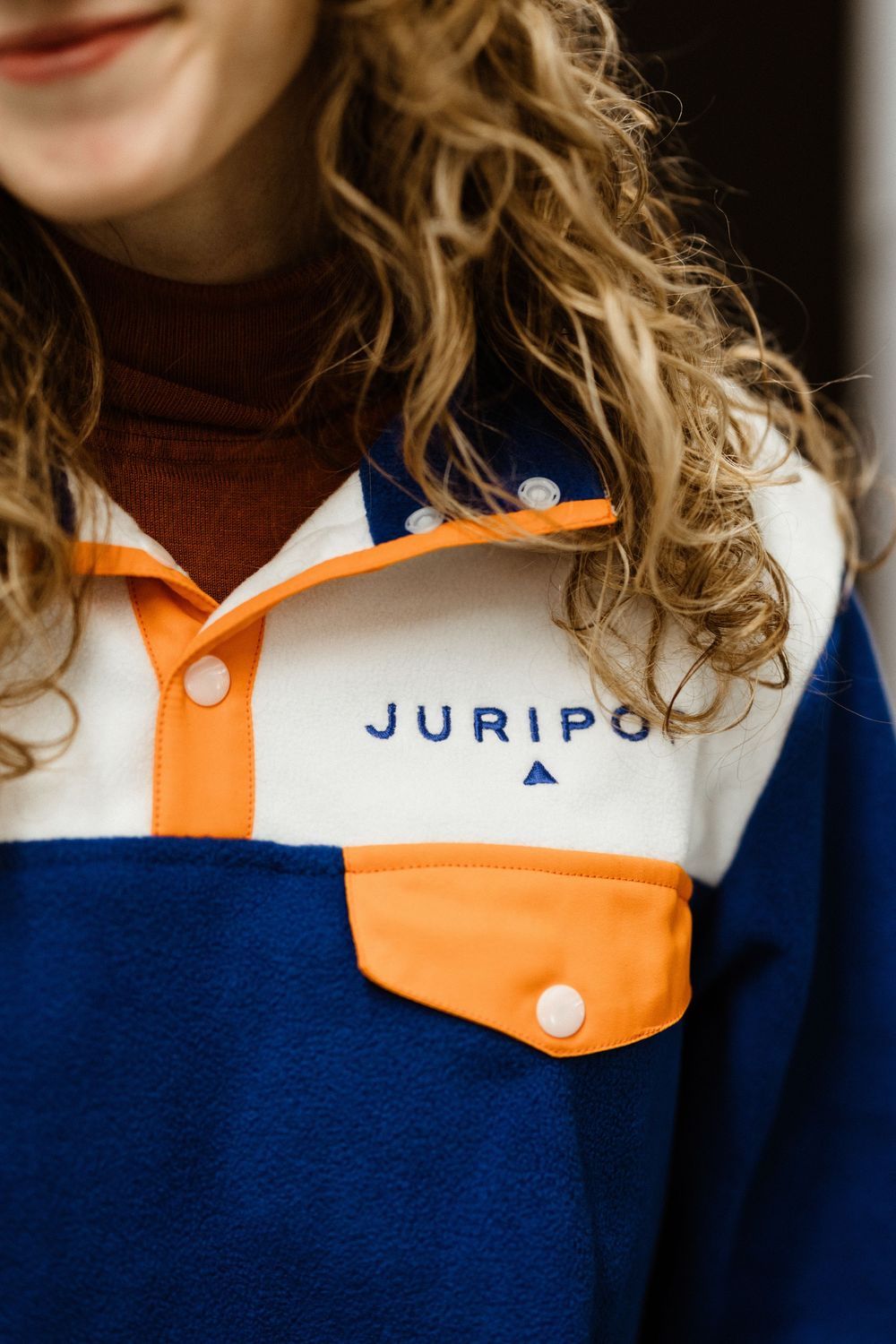 Person wearing a white, orange and navy blue color-blocked JURIPO sportswear top with contrasting panels.