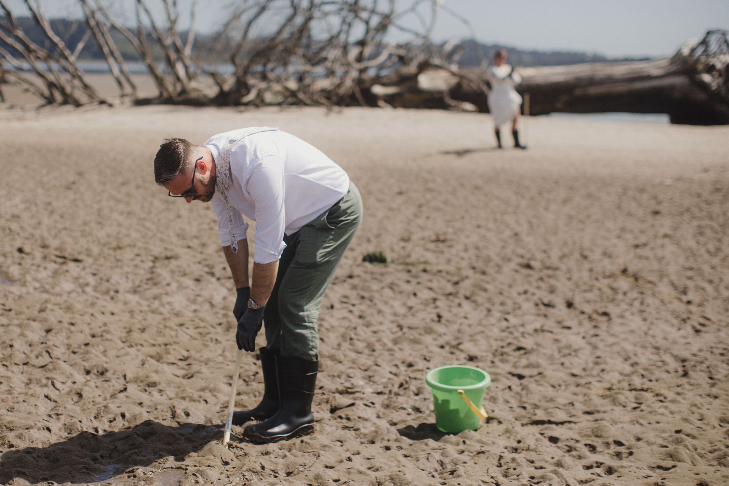 Wedding party playing beach games with buckets and shovels on a sunny shoreline.