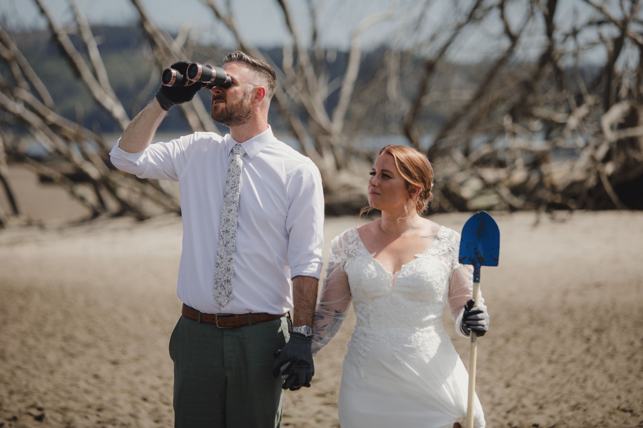 Wedding party celebrating on a beach with driftwood and trees in the background.