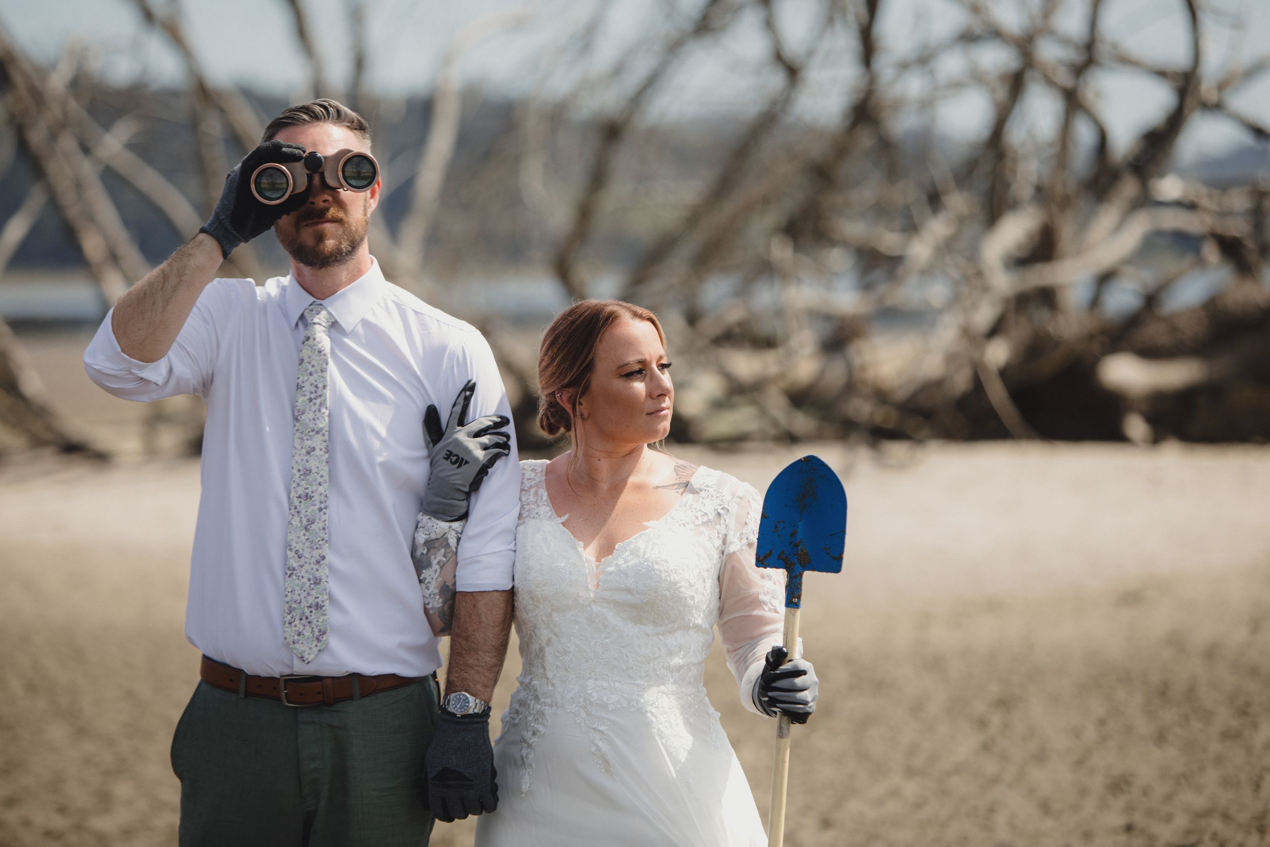 Newlyweds enjoying playful moments among driftwood on a scenic beach during their wedding celebration.