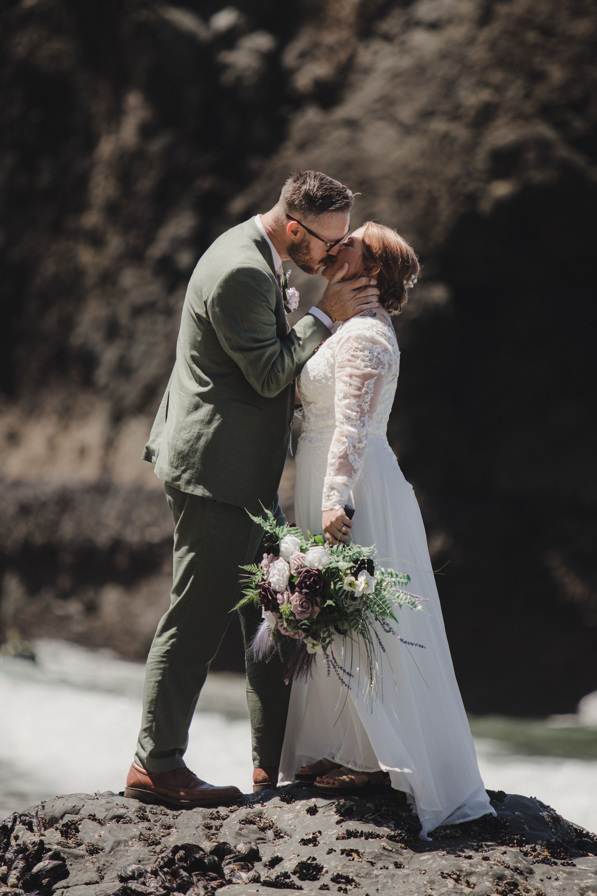 Romantic newlyweds share intimate moments on a rocky beach with dramatic cliffs in the background.