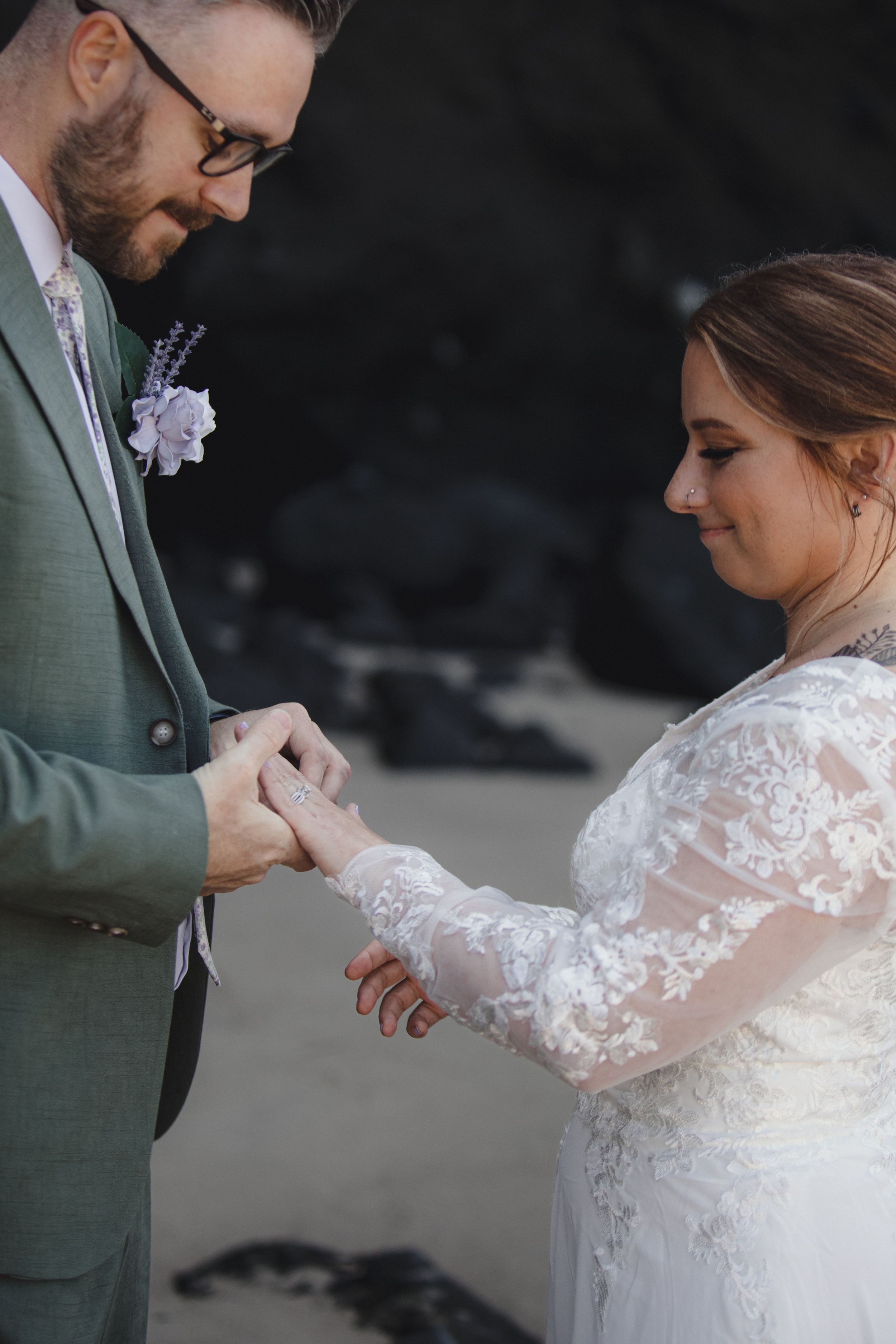 Close-up of wedding rings being exchanged with delicate lace sleeve details.