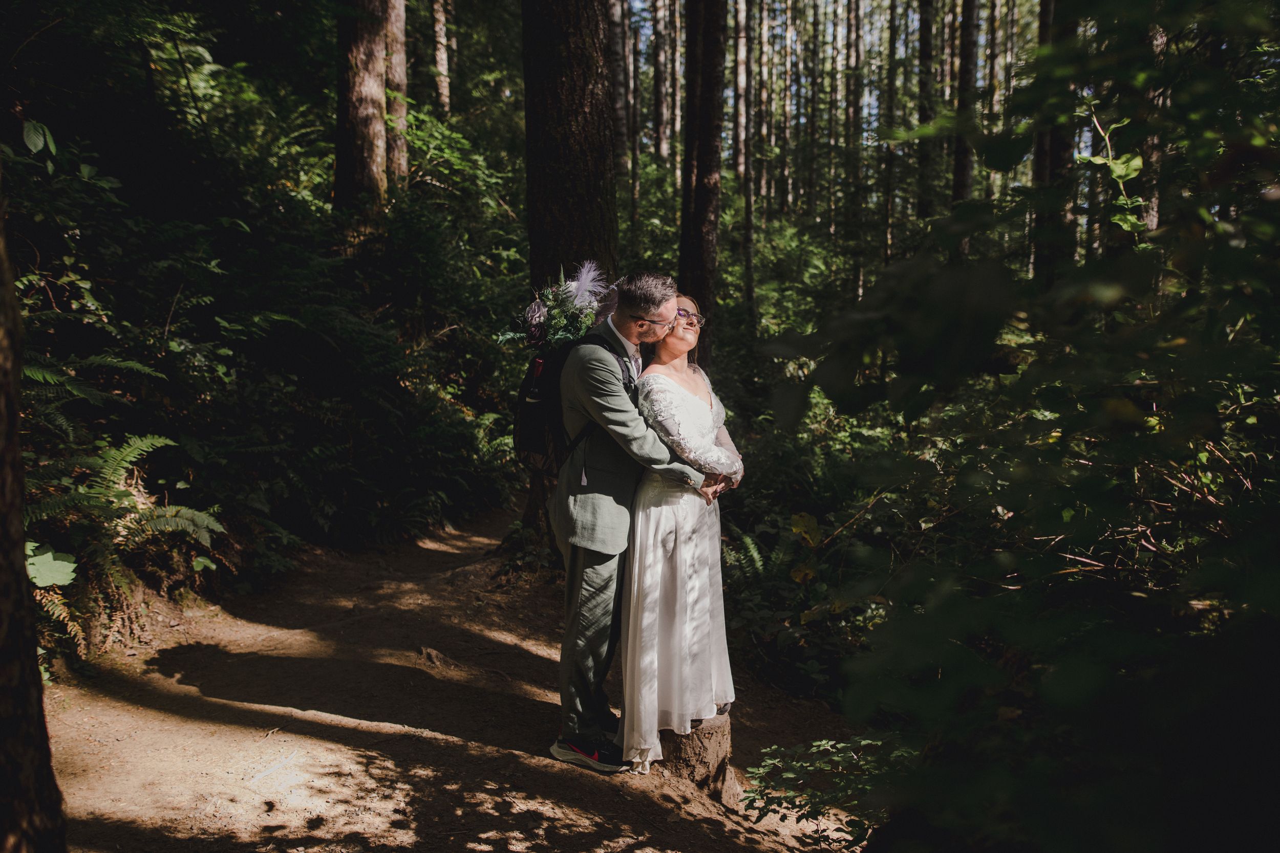 Intimate embrace on forest trail surrounded by tall evergreen trees.
