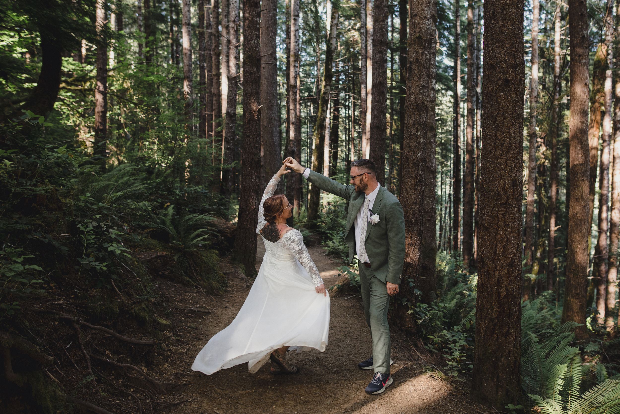 White dress twirling on forest path among tall pine trees.