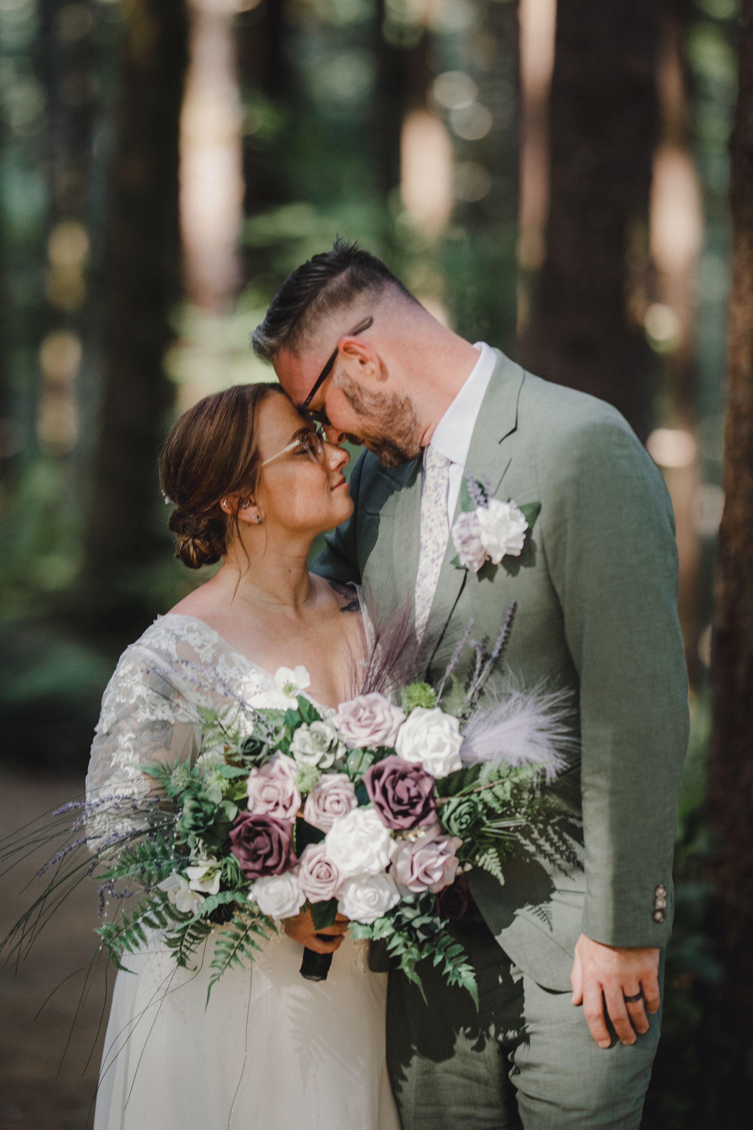 Wedding portrait in a sunlit forest with a stunning purple and white bouquet.