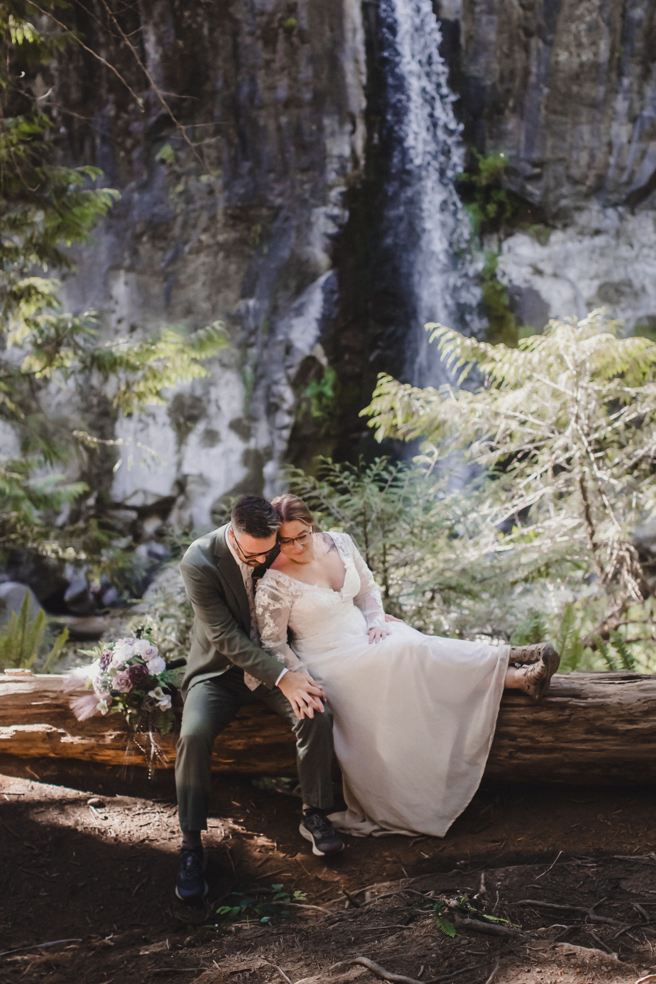Romantic moment on fallen log with majestic waterfall cascading in background.