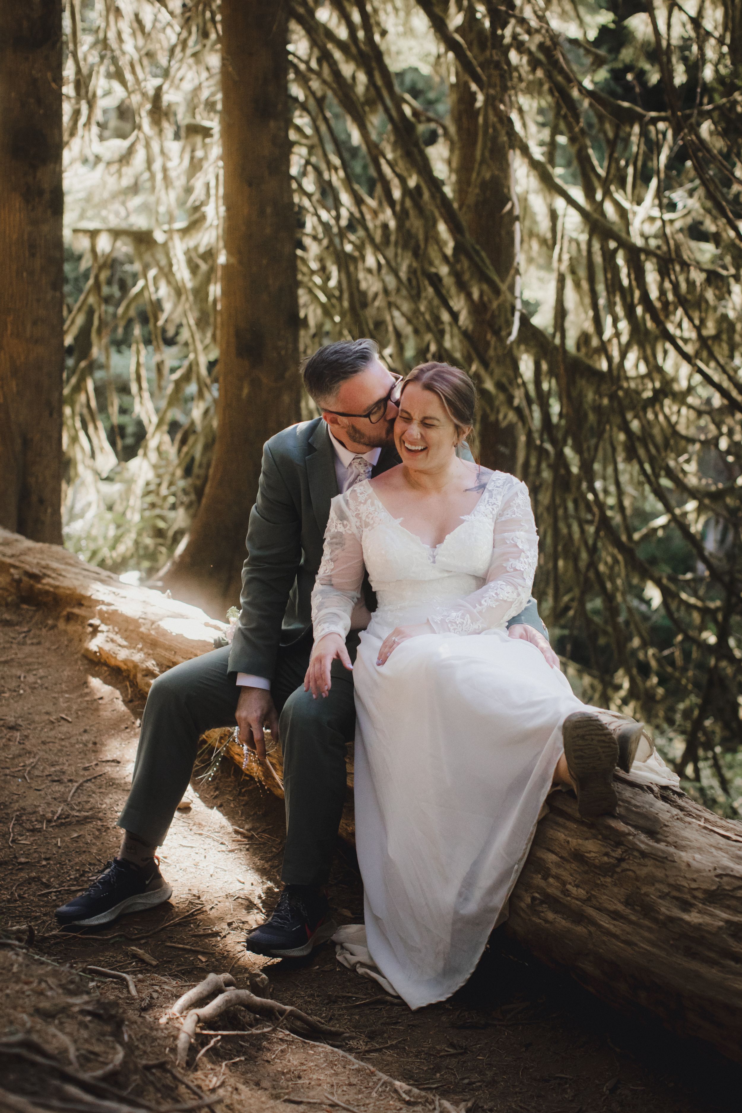 Couple shares tender moment while sitting on fallen log in sunlit forest.