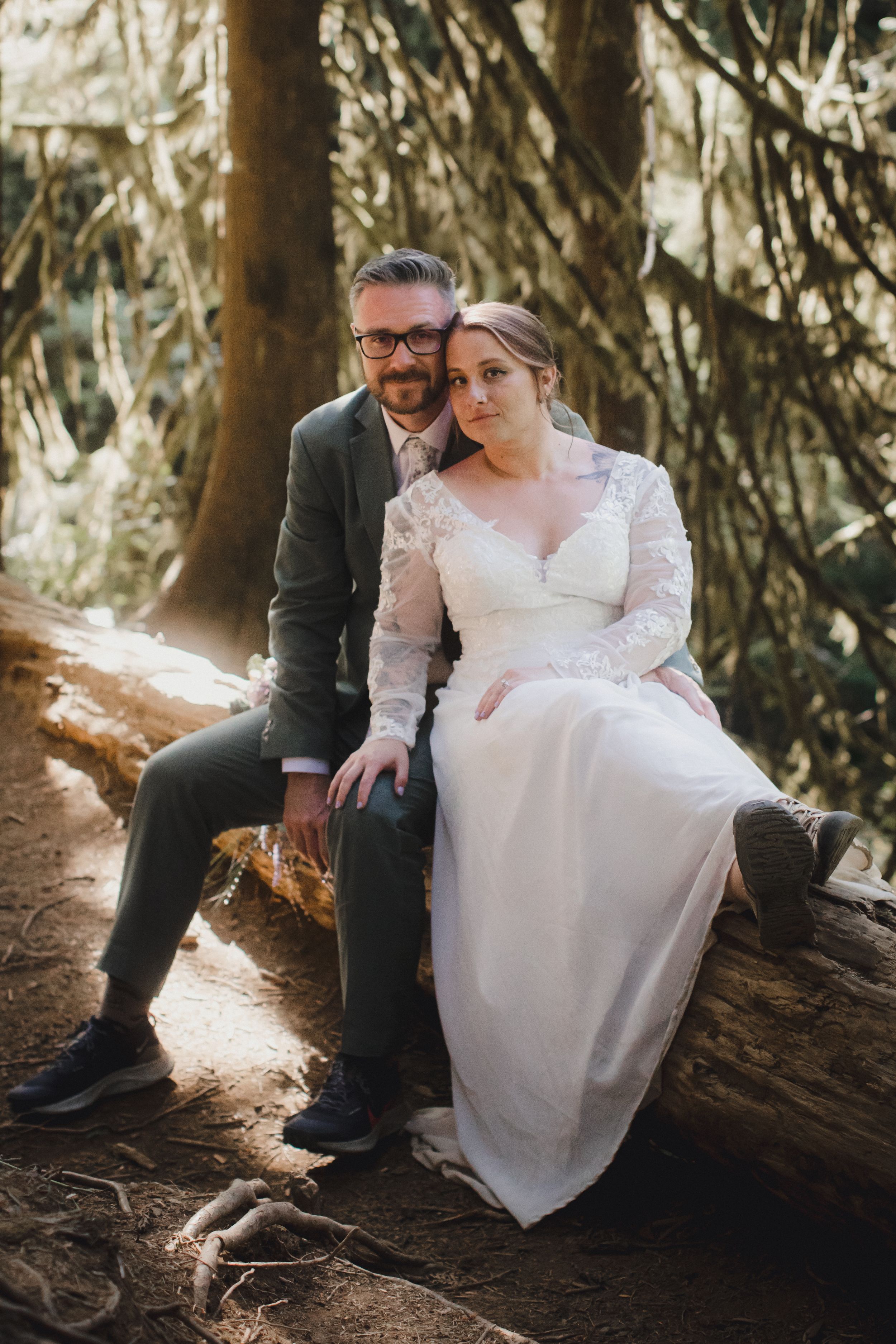 Intimate wedding photos taken on fallen log in enchanted forest setting with natural lighting.