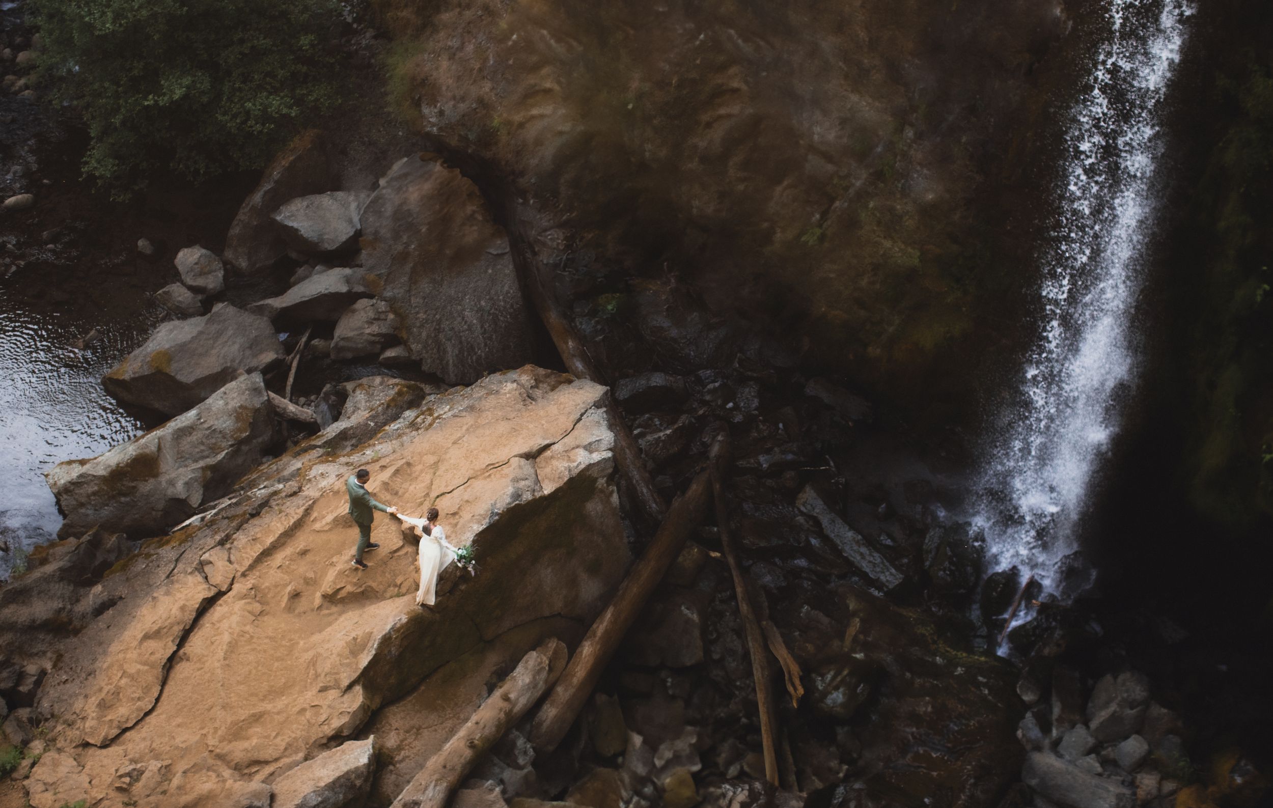A waterfall cascades down rocky cliffs near scattered driftwood on a rugged beach.