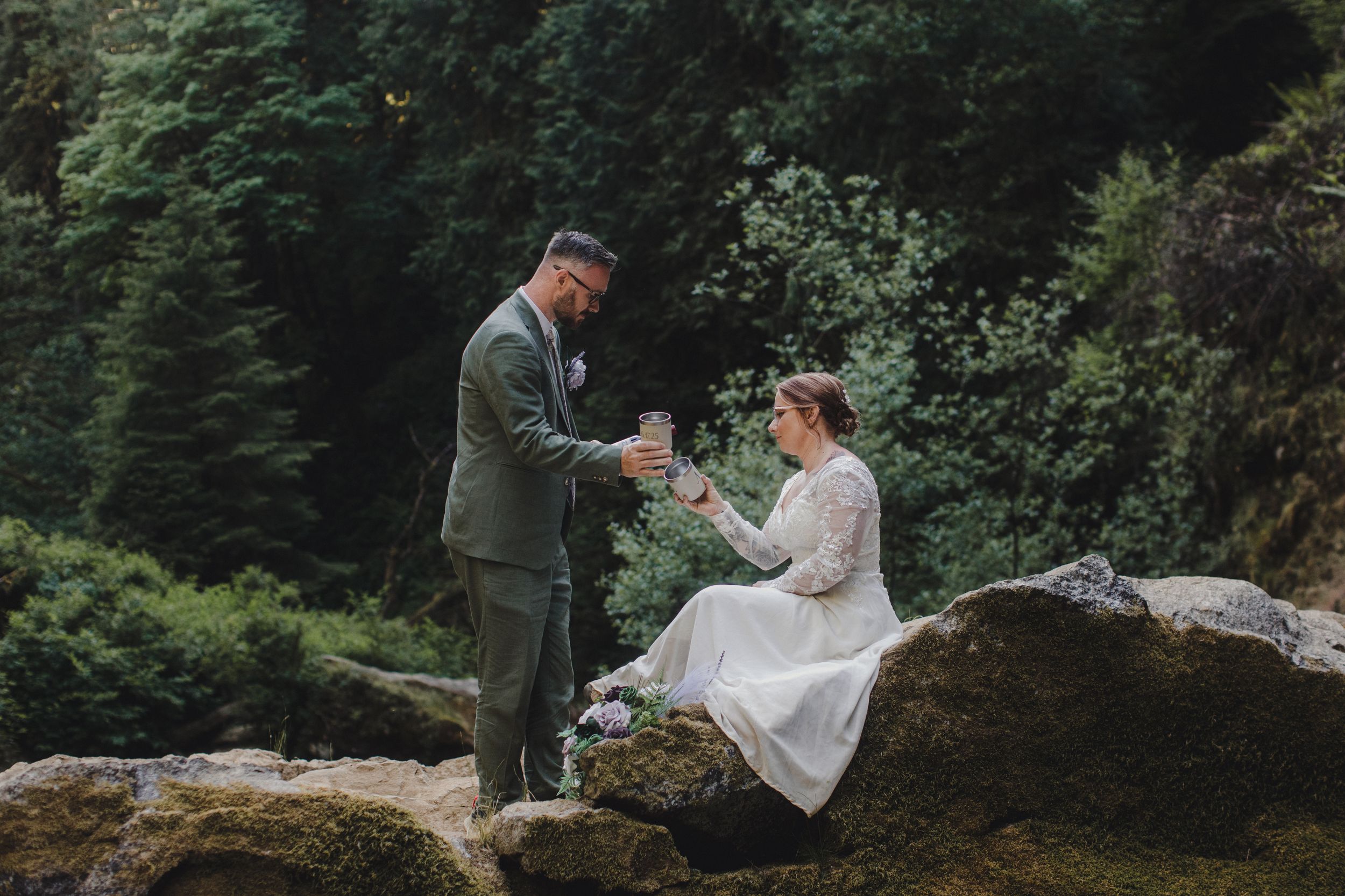 Couple shares intimate moment on rocky ledge in forest setting.