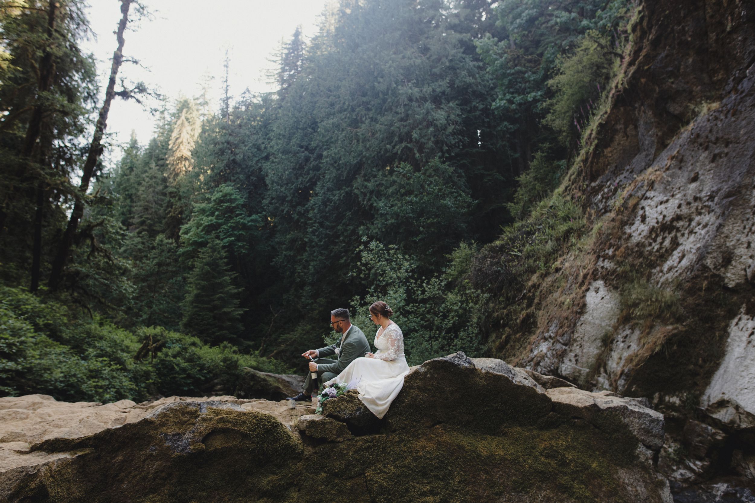 Wedding photography session in mossy Pacific Northwest forest with waterfall and cliffs.