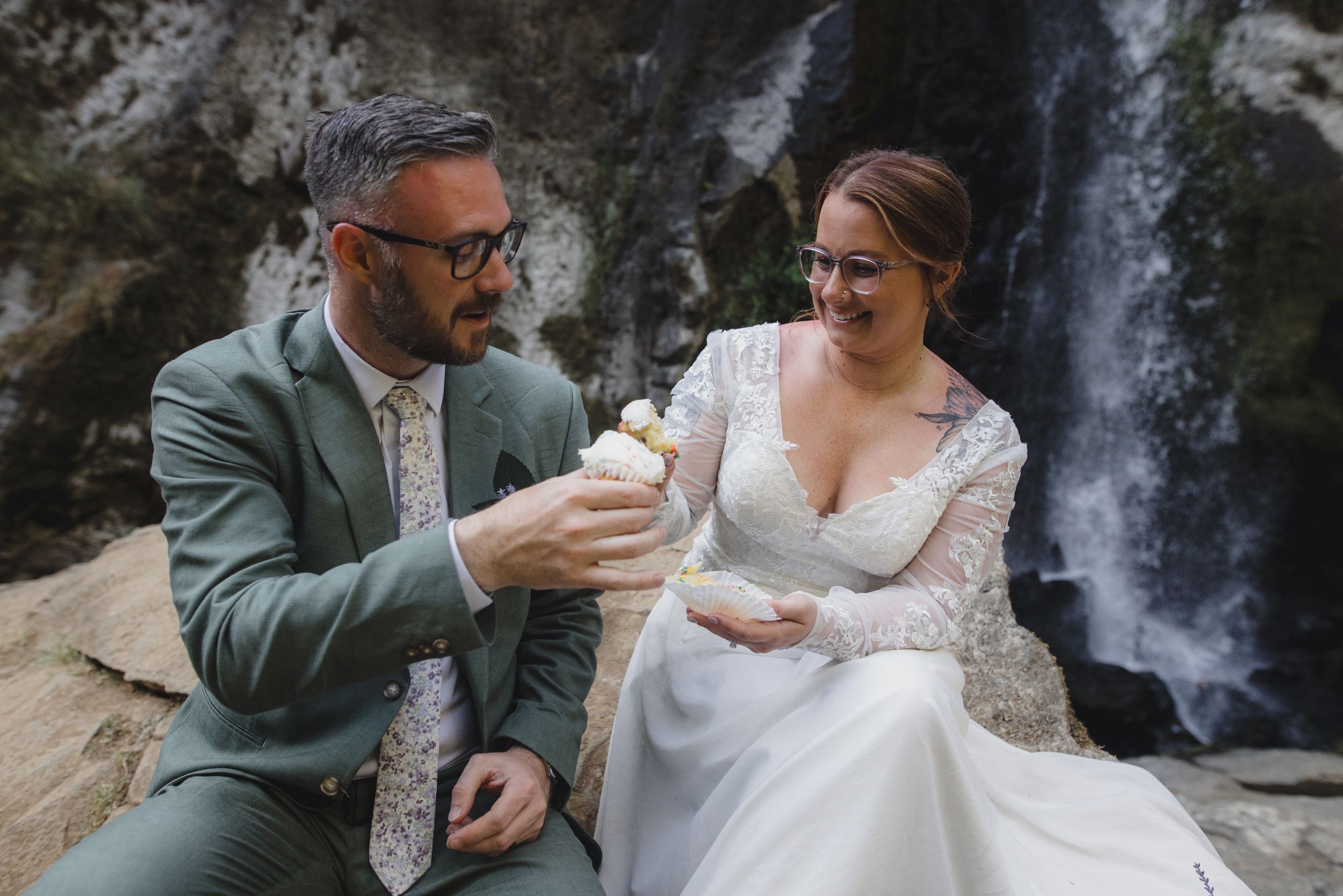Wedding couple poses by cascading waterfall in scenic forest location.