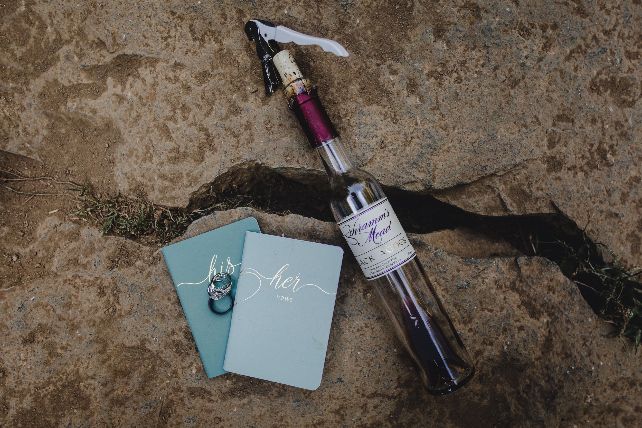 Wedding details including blue place cards and wine bottle arranged on textured stone surface.