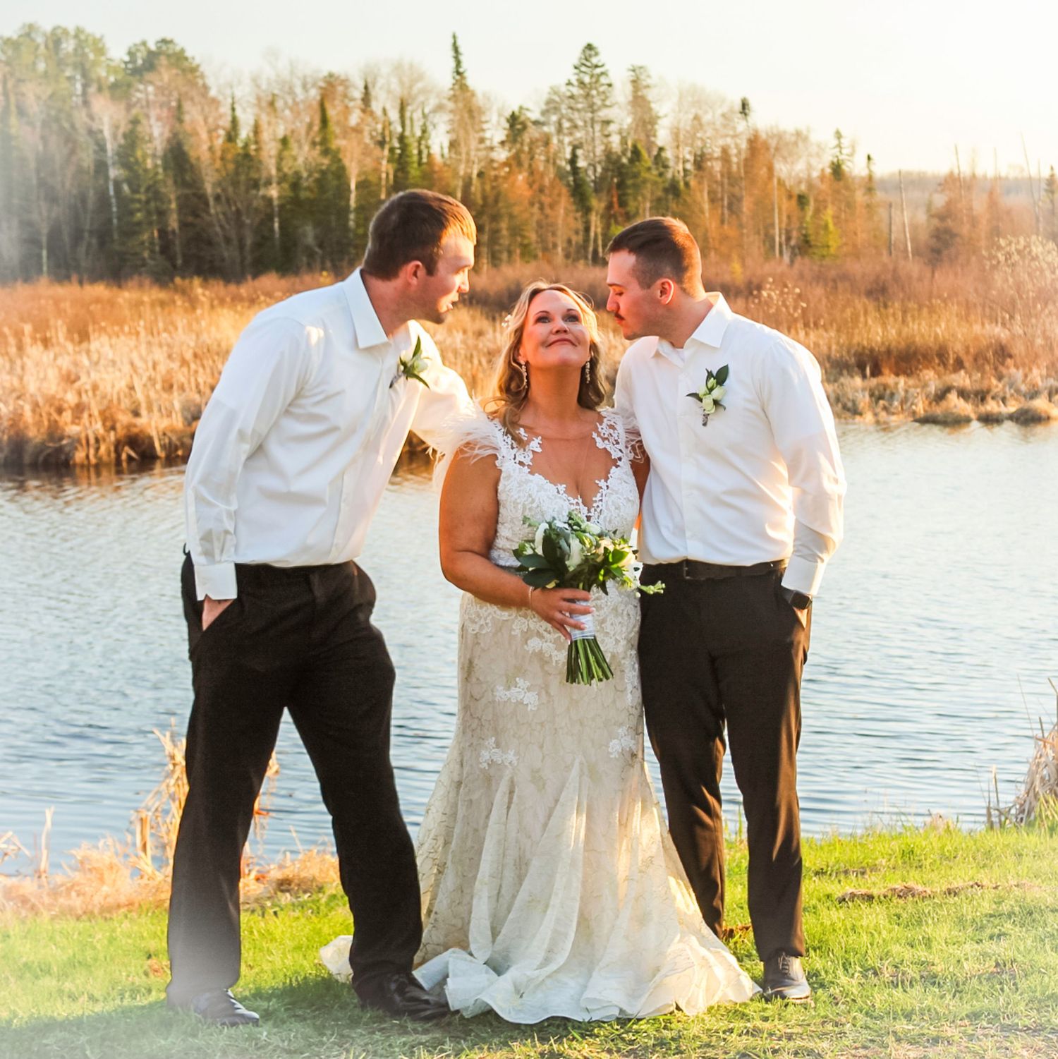 Wedding party poses for pictures near serene waterfront during golden hour at lakeside ceremony.