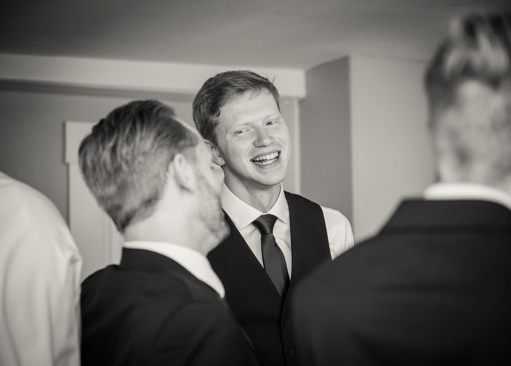 A candid black and white moment of laughter and joy shared between wedding guests in formal attire.