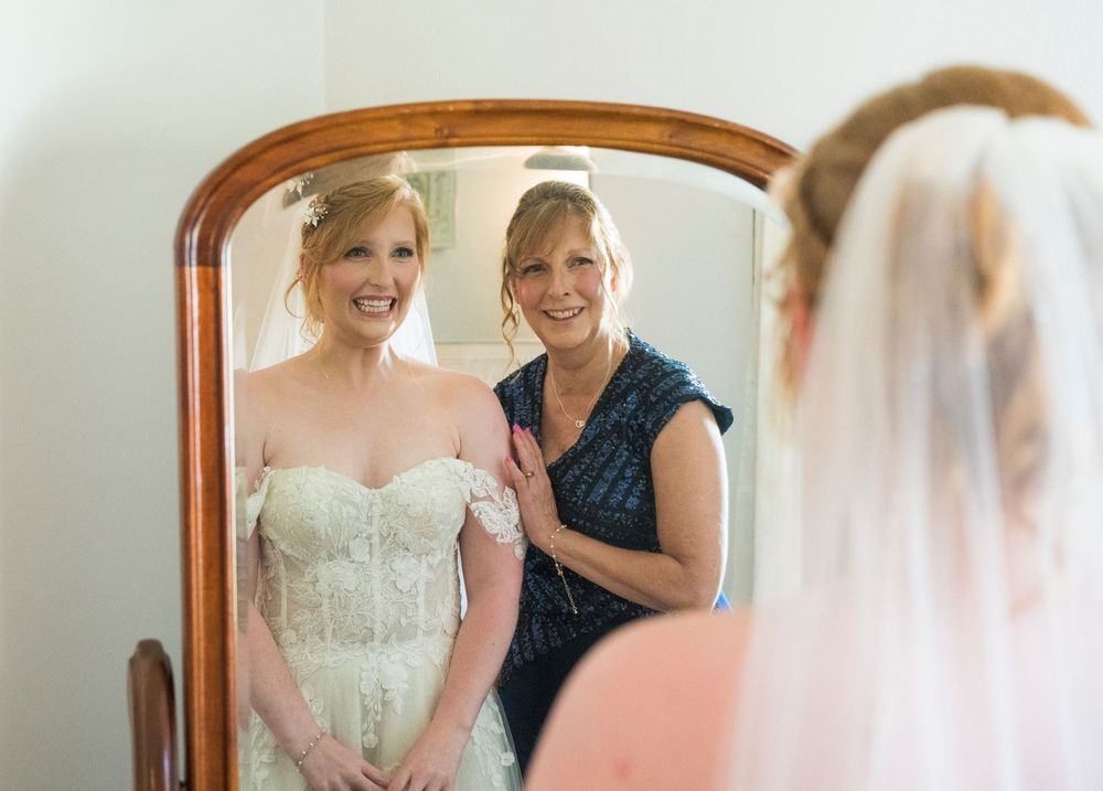 Bridal preparation moments with final dress adjustments and teal bridesmaid dress in mirror reflection.