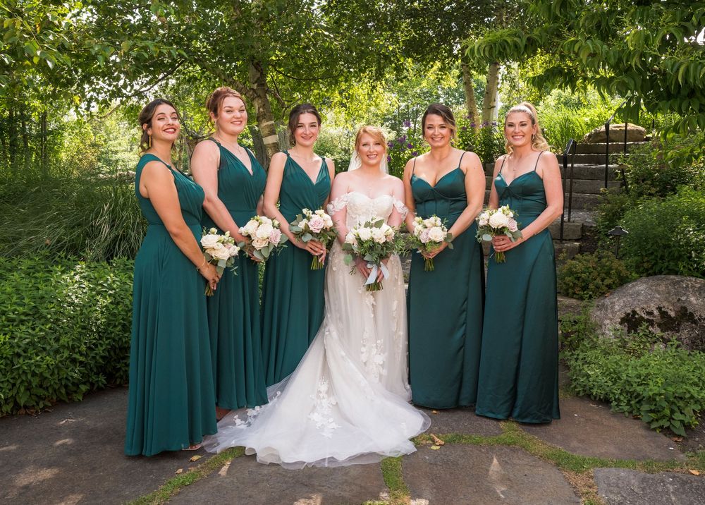 Bridal party wearing teal dresses poses together in a garden setting.