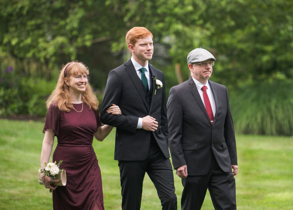 Wedding party members in formal attire walking together on green grass during an outdoor celebration.