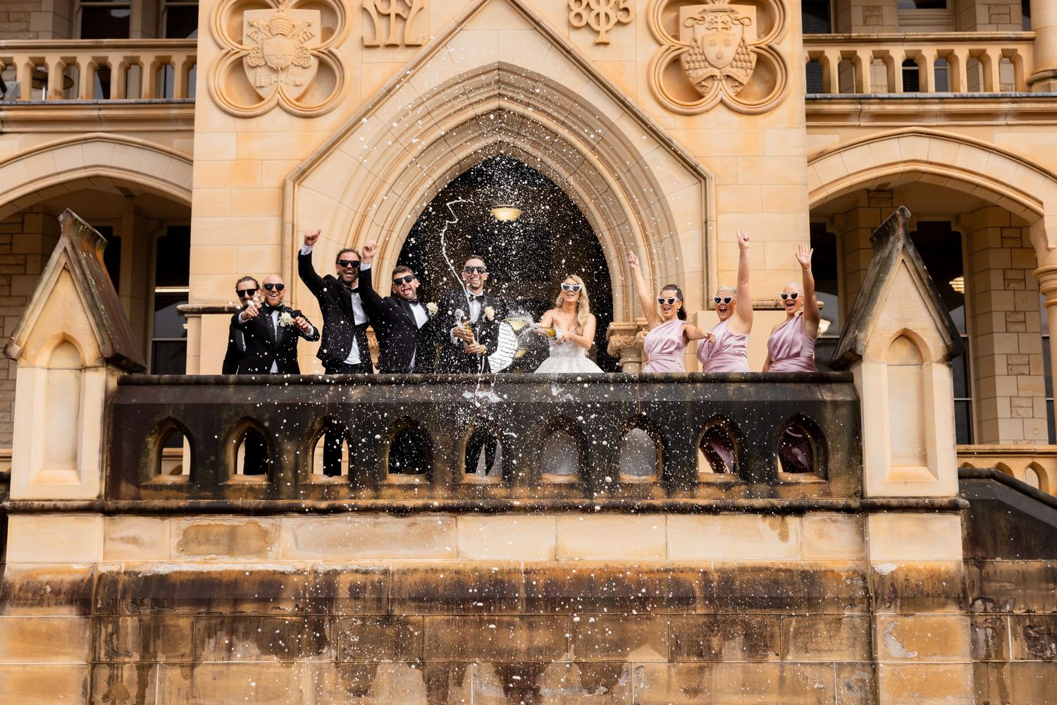 Wedding party celebrating on a gothic architectural balcony with ornate stone details.