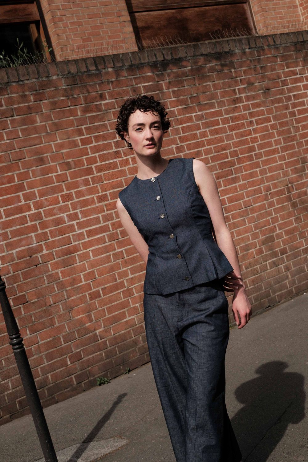 Fashion model poses stylishly against brick wall wearing sleek navy jumpsuit in urban photoshoot.