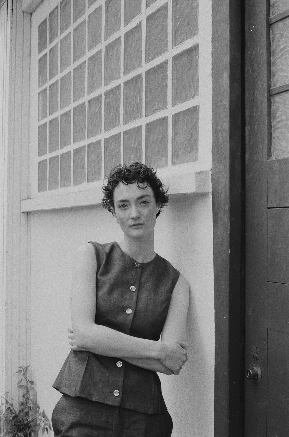 A woman in a dark sleeveless shift dress poses elegantly near windows in a vintage black and white photograph.
