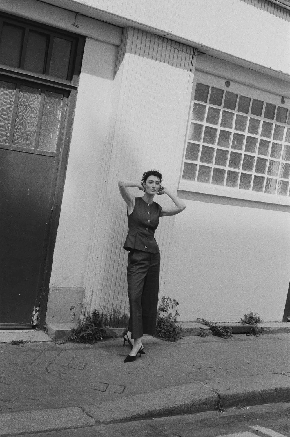 A person performs a playful sequence against a white building wall, showing energetic dance-like movements in black and white.