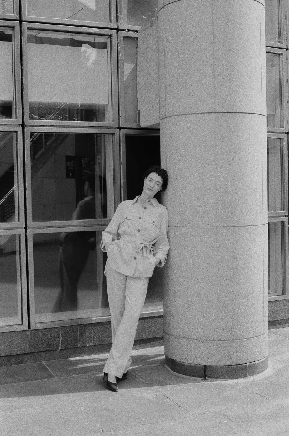 Black and white photo showing four sequential images of a person leaning against a cylindrical building pillar.