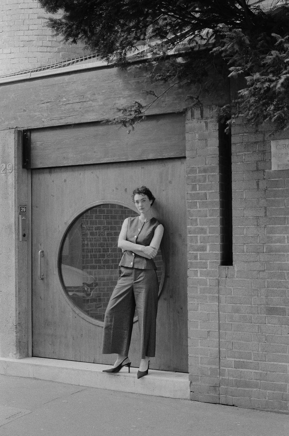 A series of five black and white photographs showing a figure emerging through circular openings in a brick wall.