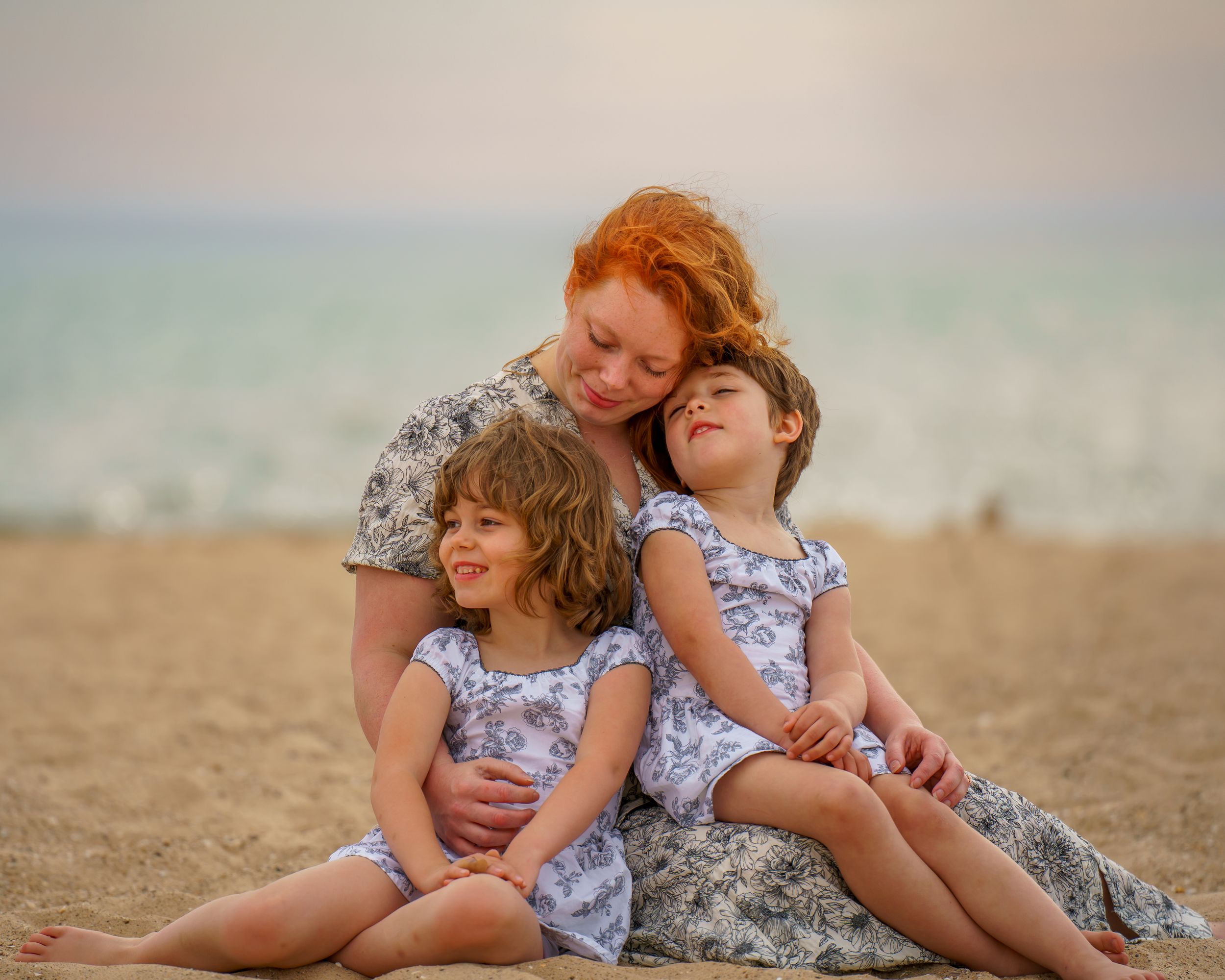Happy family sits together on sandy path surrounded by tall beach grass on summer day at dunes.