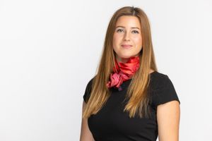 Professional portrait of woman wearing a black top and bright red scarf against white background.
