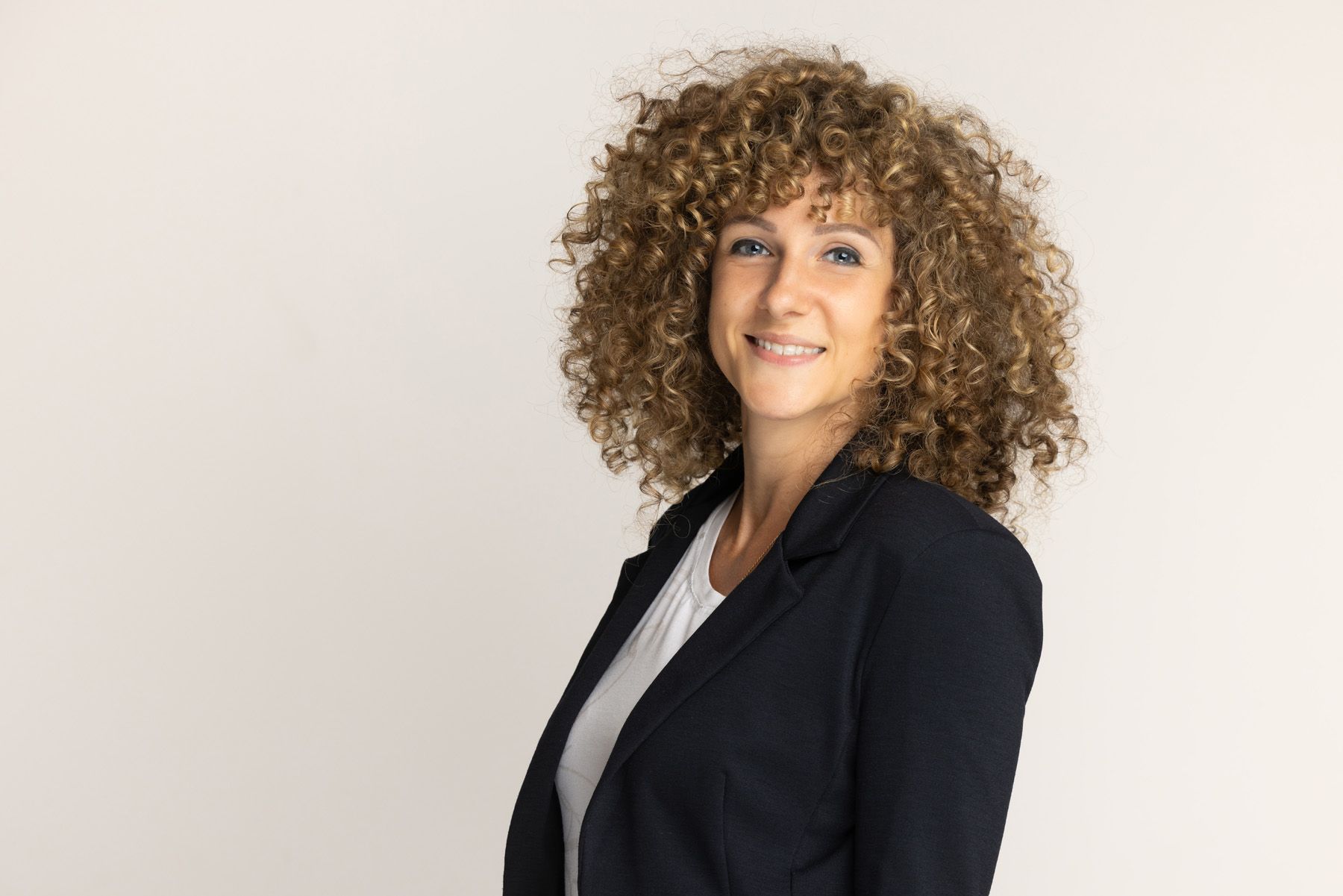 Professional portrait wearing a black blazer with natural curly hair against a light background.